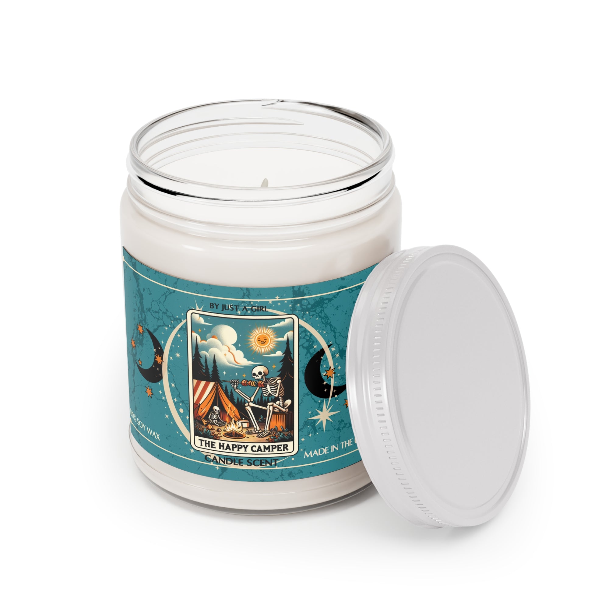 Eine weiße Kerze in einem durchsichtigen Glasgefäß mit weißem Deckel. Das Etikett ist türkisblau mit Mond- und Sternmotiven und zeigt in der Mitte eine goldgerahmte Illustration. Darauf ist ein Skelett zu sehen, das vor einem Zelt an einem Lagerfeuer sitzt und Gitarre spielt, unter einer lachenden Sonne. Über dem Skelett ist ein sternenklarer Nachthimmel mit einem Vollmond und Noten zu sehen. Der Text auf dem Etikett lautet "BY JUST A GIRL".