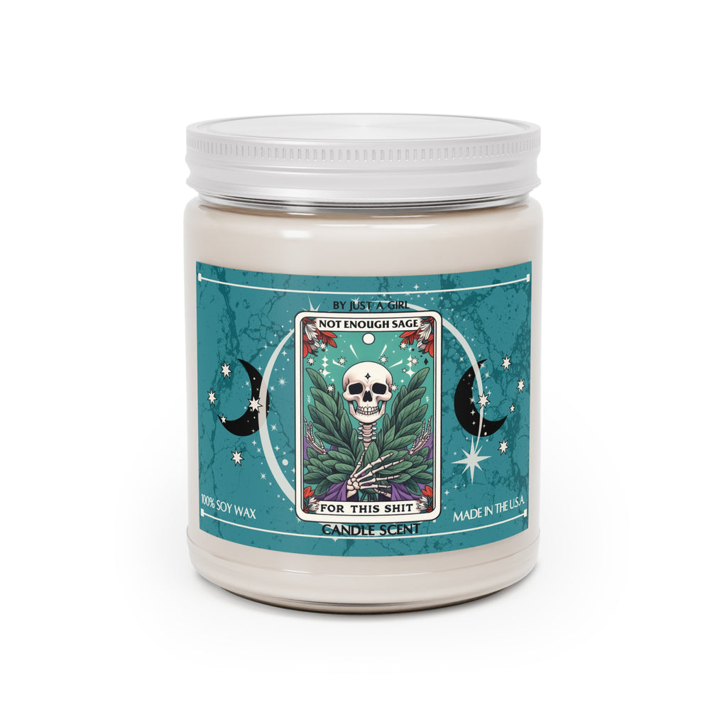 Eine weiße Kerze in einem durchsichtigen Glasgefäß mit weißem Deckel. Das Etikett ist türkisblau mit Mond- und Sternmotiven und zeigt in der Mitte eine goldgerahmte Illustration. Darauf ist ein Totenkopf zu sehen, umgeben von grünen Salbeiblättern und kleinen roten Blüten. Der Text auf dem Etikett lautet "BY JUST A GIRL".