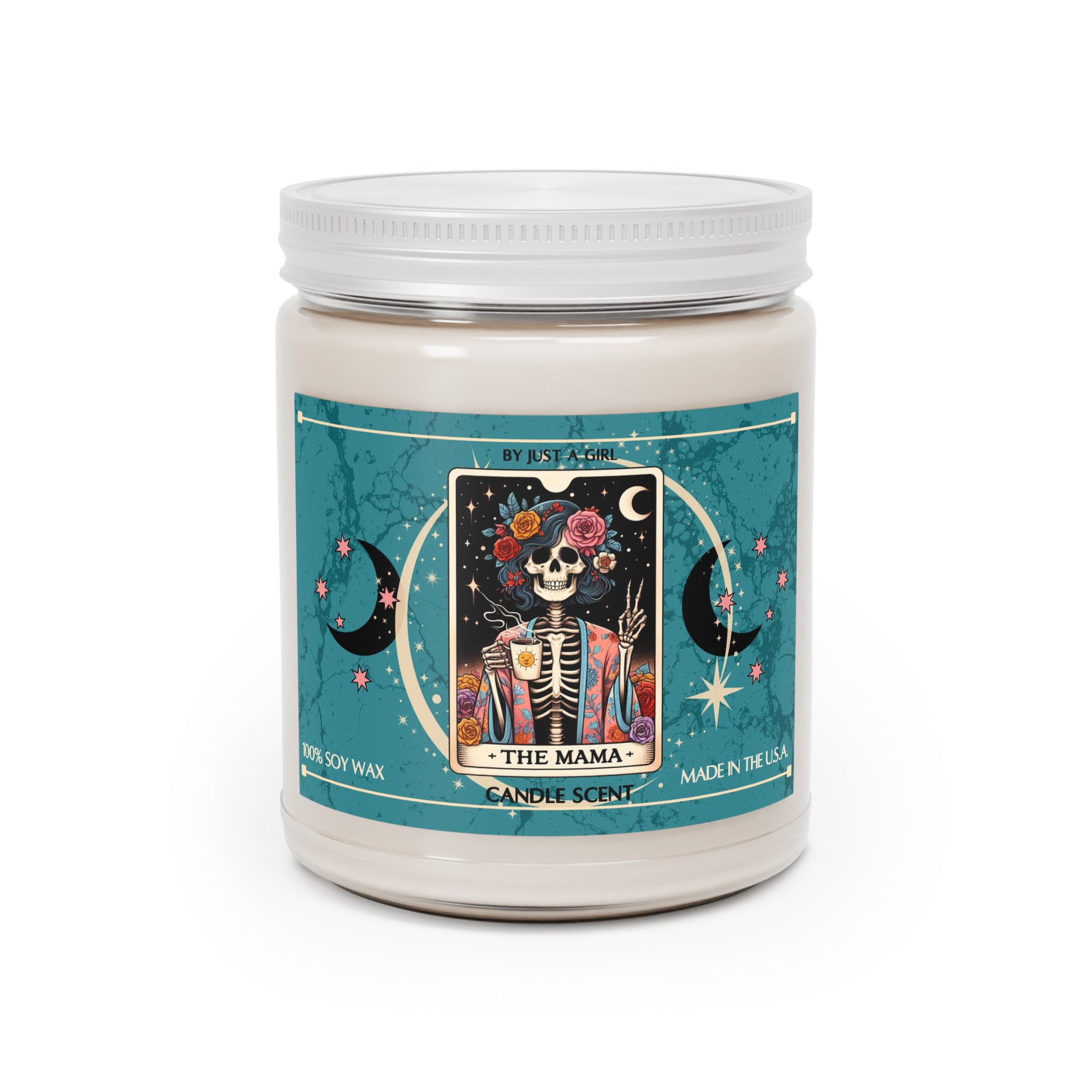 Eine weiße Kerze in einem durchsichtigen Glasgefäß mit weißem Deckel. Das Etikett ist türkisblau mit Mond- und Sternmotiven und zeigt in der Mitte eine goldgerahmte Illustration. Darauf ist ein lächelndes Skelett mit Blumen im Haar und einem bunten Blumenmuster auf der Robe zu sehen, das eine Tasse Kaffee hält und einen Peace-Zeichen mit der anderen Hand macht. Der Text auf dem Etikett lautet "BY JUST A GIRL", "THE MAMA" und "CANDLE SCENT". Unten steht "100% SOY WAX" und "MADE IN THE U.S.A.".