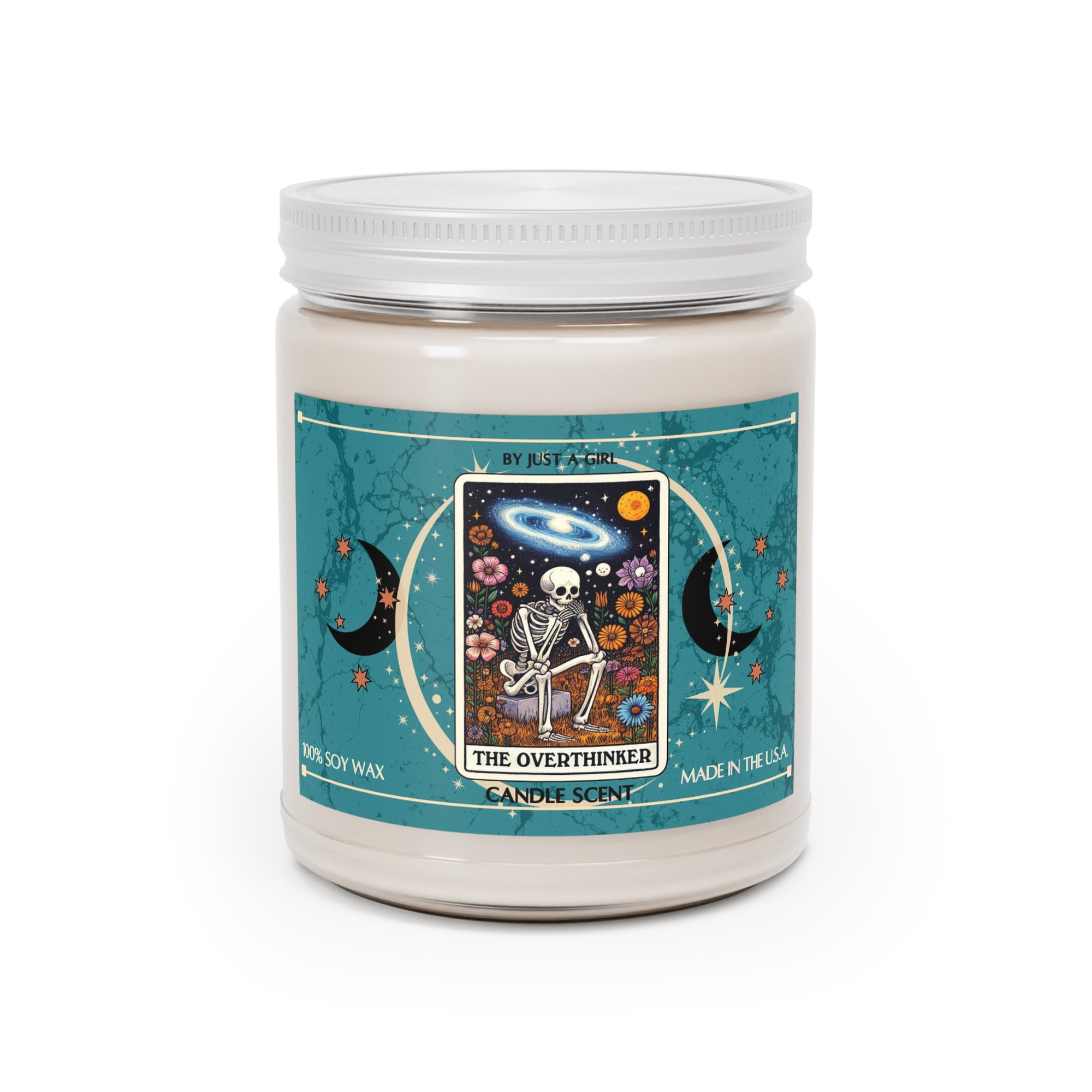Eine weiße Kerze in einem durchsichtigen Glasgefäß mit weißem Deckel. Das Etikett ist türkisblau mit Mond- und Sternmotiven und zeigt in der Mitte eine goldgerahmte Illustration. Darauf ist ein Skelett zu sehen, das mit gekreuzten Beinen inmitten eines Feldes bunter Blumen sitzt und nachdenklich in den Nachthimmel mit Sternen, Planeten und einer Galaxie blickt. Der Text auf dem Etikett lautet "BY JUST A GIRL"
