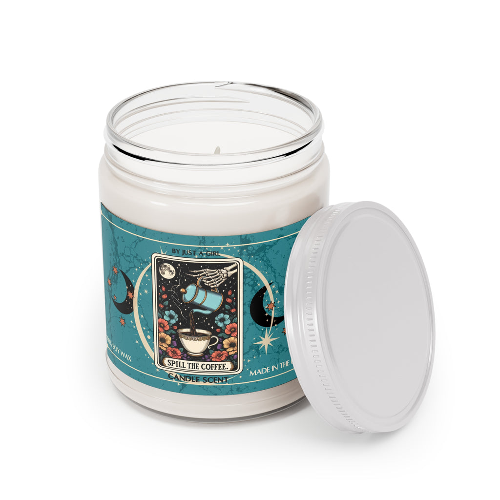 Eine weiße Kerze in einem durchsichtigen Glasgefäß mit weißem Deckel. Das Etikett ist türkisblau mit Mond- und Sternmotiven und zeigt in der Mitte eine goldgerahmte Illustration. Darauf ist ein Skelettarm zu sehen, der eine türkisfarbene Kanne hält, aus der Kaffee in eine weiße Tasse gegossen wird. Die Tasse steht auf einer Blumenwiese unter einem Vollmond. Der Text auf dem Etikett lautet "BY JUST A GIRL"