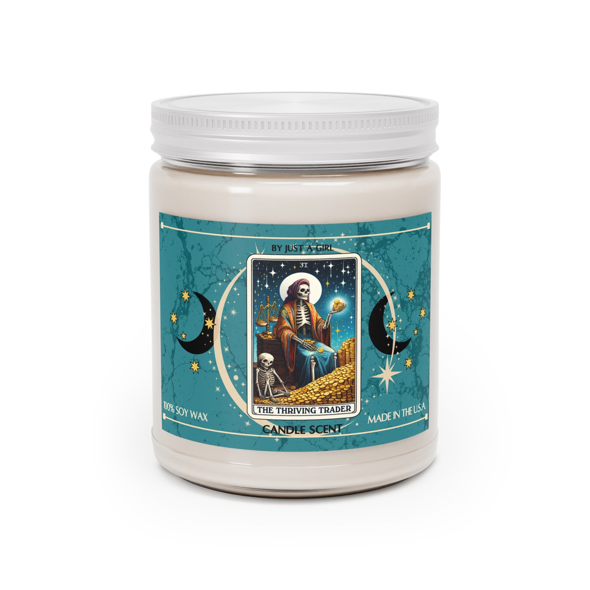 Eine weiße Kerze in einem durchsichtigen Glasgefäß mit weißem Deckel. Das Etikett ist türkisblau mit Mond- und Sternmotiven und zeigt in der Mitte eine goldgerahmte Illustration. Darauf ist ein sitzendes Skelett mit Waage und Gold in der Hand zu sehen, umgeben von einem Berg Goldmünzen und einem kleineren Skelett. Der Text auf dem Etikett lautet "BY JUST A GIRL", "31", "THE THRIVING TRADER" und "CANDLE SCENT". Unten steht "100% SOY WAX" und "MADE IN THE U.S.A.".