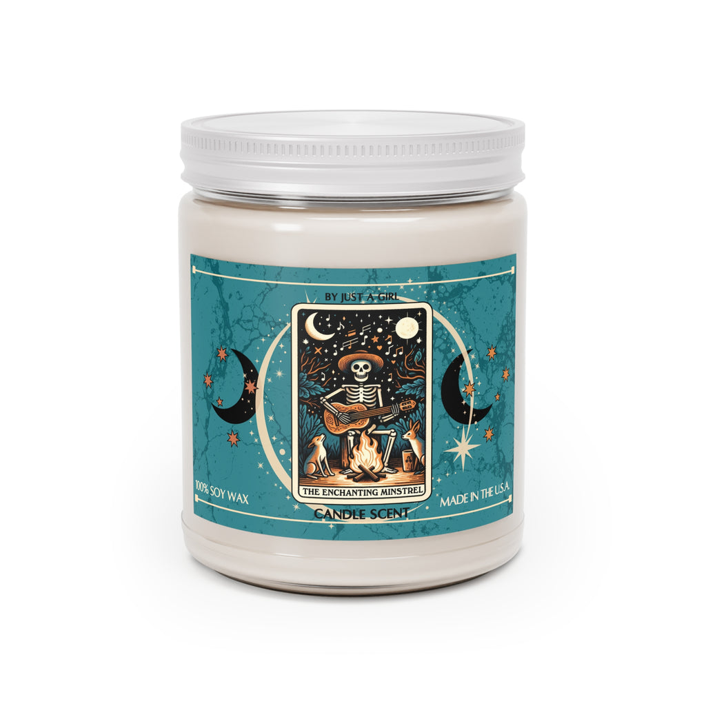Eine weiße Kerze in einem durchsichtigen Glasgefäß mit weißem Deckel. Das Etikett ist türkisblau mit Mond- und Sternmotiven und zeigt in der Mitte eine goldgerahmte Illustration. Darauf ist ein sitzendes Skelett mit Hut zu sehen, das Gitarre spielt, während es an einem Lagerfeuer sitzt. Zwei kleine Hunde oder Füchse sitzen daneben. Über dem Skelett ist ein sternenklarer Nachthimmel mit einem Vollmond und Noten zu sehen.