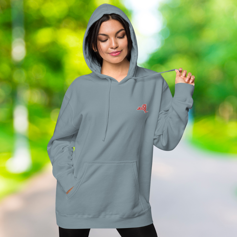 Ein weibliches Model zeigt lässig tragend den "New York" Kapuzenpullover in Schiefer blau  Vorderansicht mit der rechten Hand in der vorderen Kängurutasche.