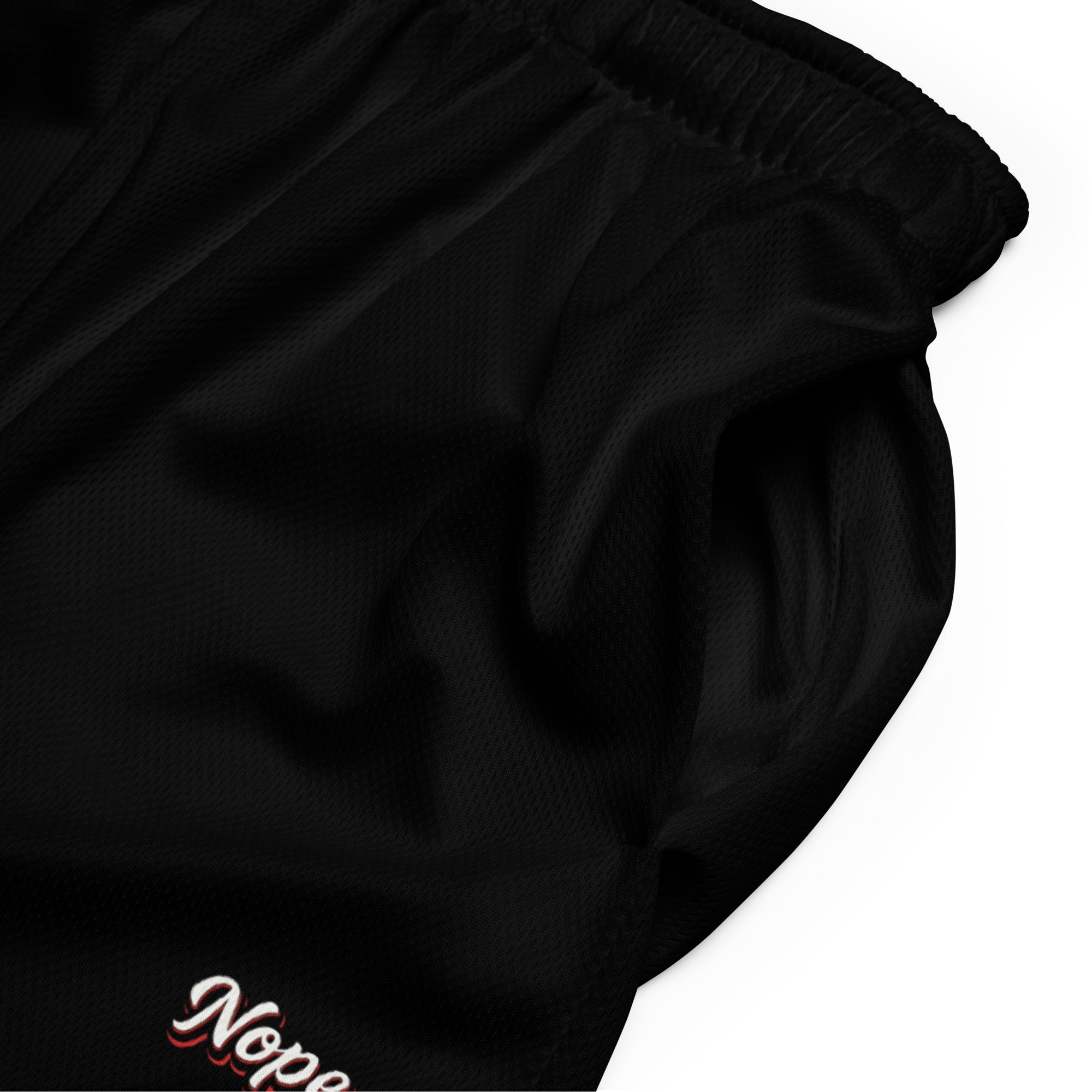 Schwarze Mesh-Sportshorts mit elastischem Bund. Am unteren rechten Bein steht in weißer Schrift mit rotem Schatten und schwarzem Rand das Wort "Nope".
