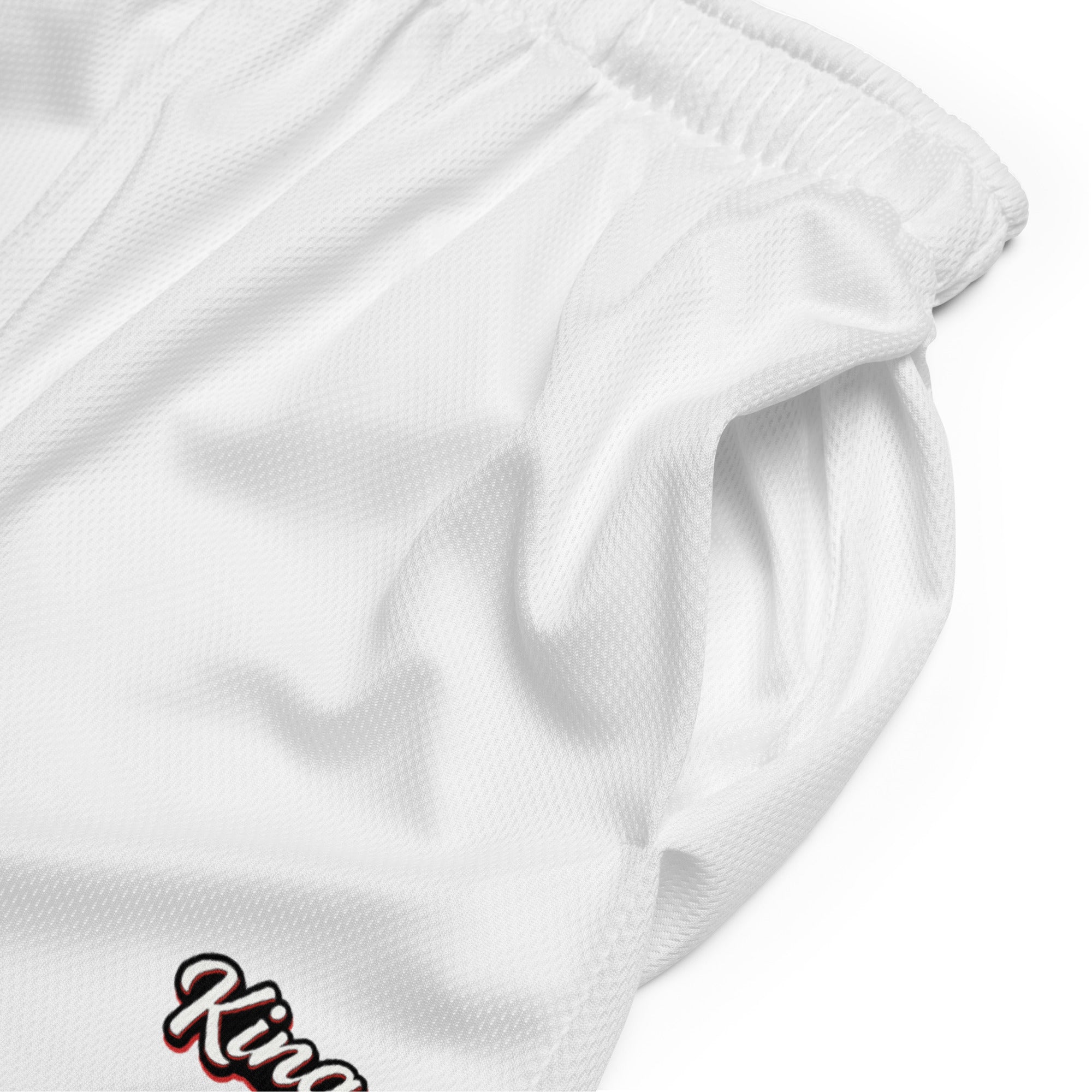 Weiße Mesh-Sportshorts mit elastischem Bund. Am unteren rechten Bein steht in schwarzer Schrift mit rotem Schatten und weißem Rand das Wort "King".