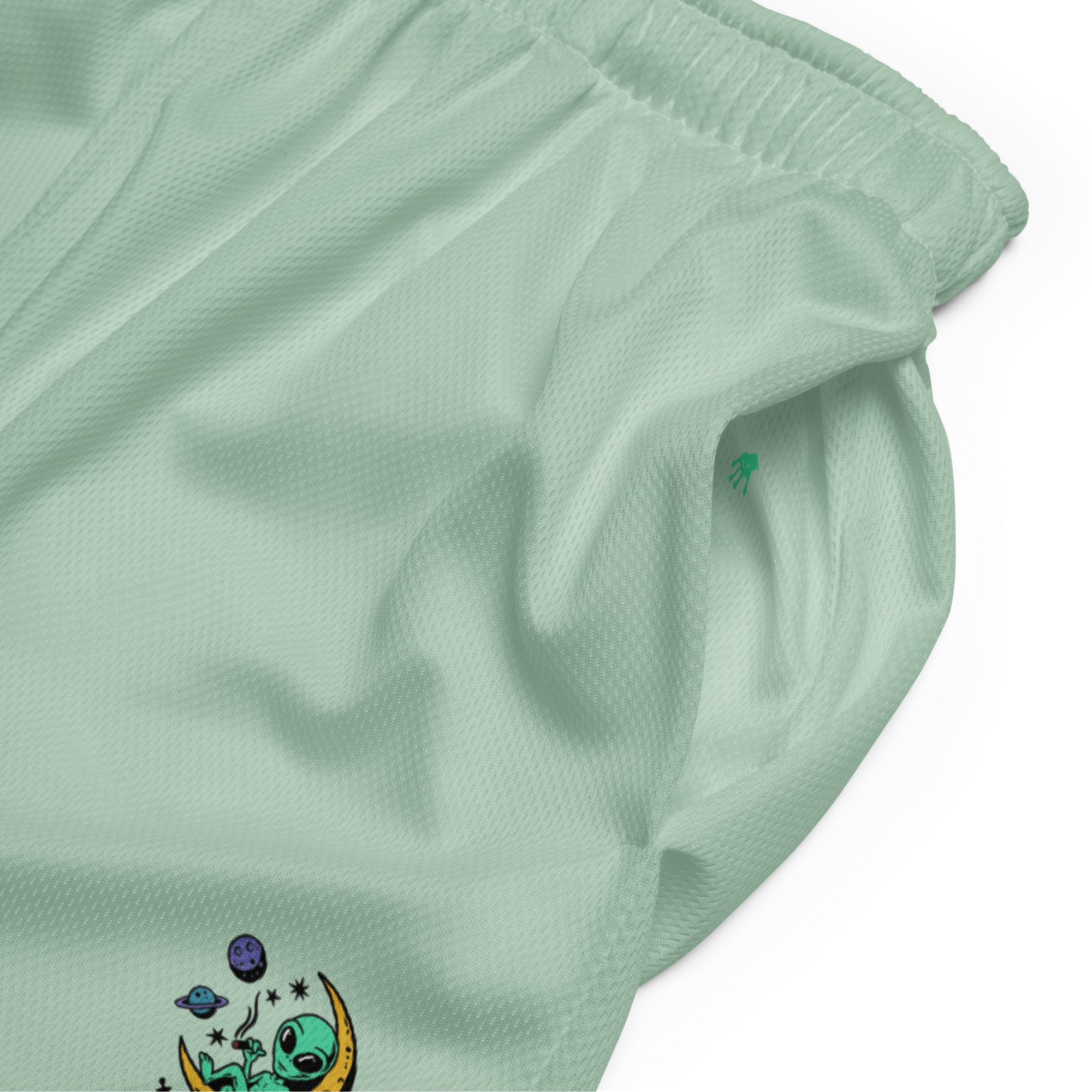 Ein Paar mintgrüne Basketballshorts, die auf dem linken Hosenbein das farbenfrohe "Chilling Vibes"-Logo mit einem grünen Alien auf einem gelben Halbmond zeigen, umgeben von Sternen und Planeten. Die Shorts bestehen aus glattem Sportmaterial.