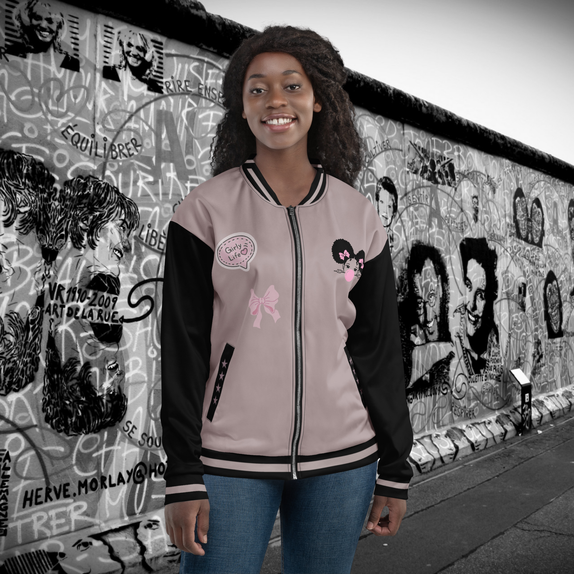 Die "Bubble Girl" Jacke im College Style gezeigt von einem weiblichen Model in der Vorderansicht. Auf der linken Brust ist ein kleines Afro Mädchen mit MM Haaren und rosa Schleifchen im Haar. Es schaut entspannt und macht eine riesen Kaugummiblase in Pink. Auf der rechten Seite sind 2 Elemente einemal eine Schleife im dezenten Style sowie ein Batch aufnäher gedruckt im Girlie Life Stil. Auf den Taschenbündchen sind jeweils dezent passende 4 Sterne zu sehen. By Just a Gril.