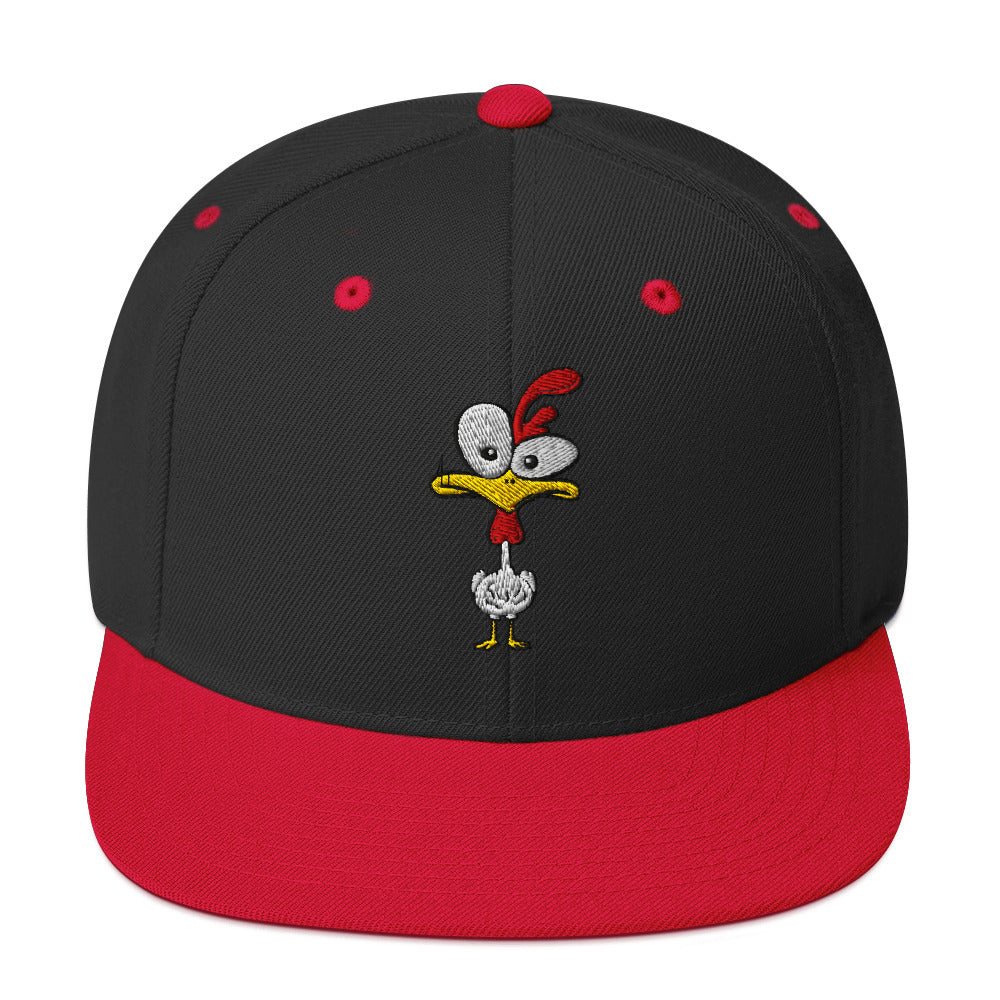 Eine klassische, zweifarbige Snapback-Cap mit flachem Schirm. Auf der Vorderseite ist ein gesticktes Cartoon-Motiv eines Huhns zu sehen, das einen hellen Kopf, große Augen, einen farbigen Kamm und einen Schnabel sowie eine kleine stilisierte Geste am Hals hat. Der obere Teil der Kappe ist dunkel, während der Schirm und der obere Knopf eine leuchtende Kontrastfarbe aufweisen.