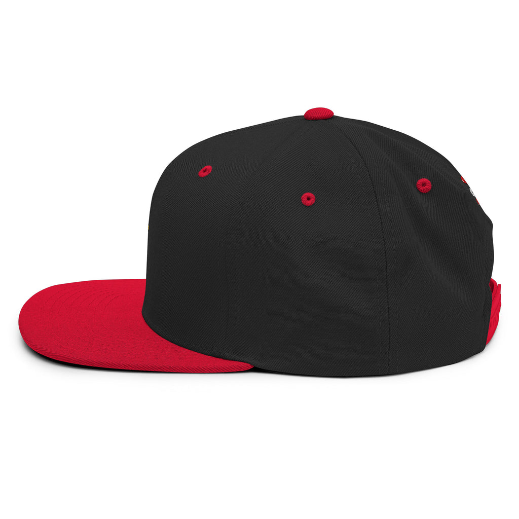 Eine klassische, zweifarbige Snapback-Cap mit flachem Schirm. Auf der Vorderseite ist ein gesticktes Cartoon-Motiv eines Huhns zu sehen, das einen hellen Kopf, große Augen, einen farbigen Kamm und einen Schnabel sowie eine kleine stilisierte Geste am Hals hat. Der obere Teil der Kappe ist dunkel, während der Schirm und der obere Knopf eine leuchtende Kontrastfarbe aufweisen.