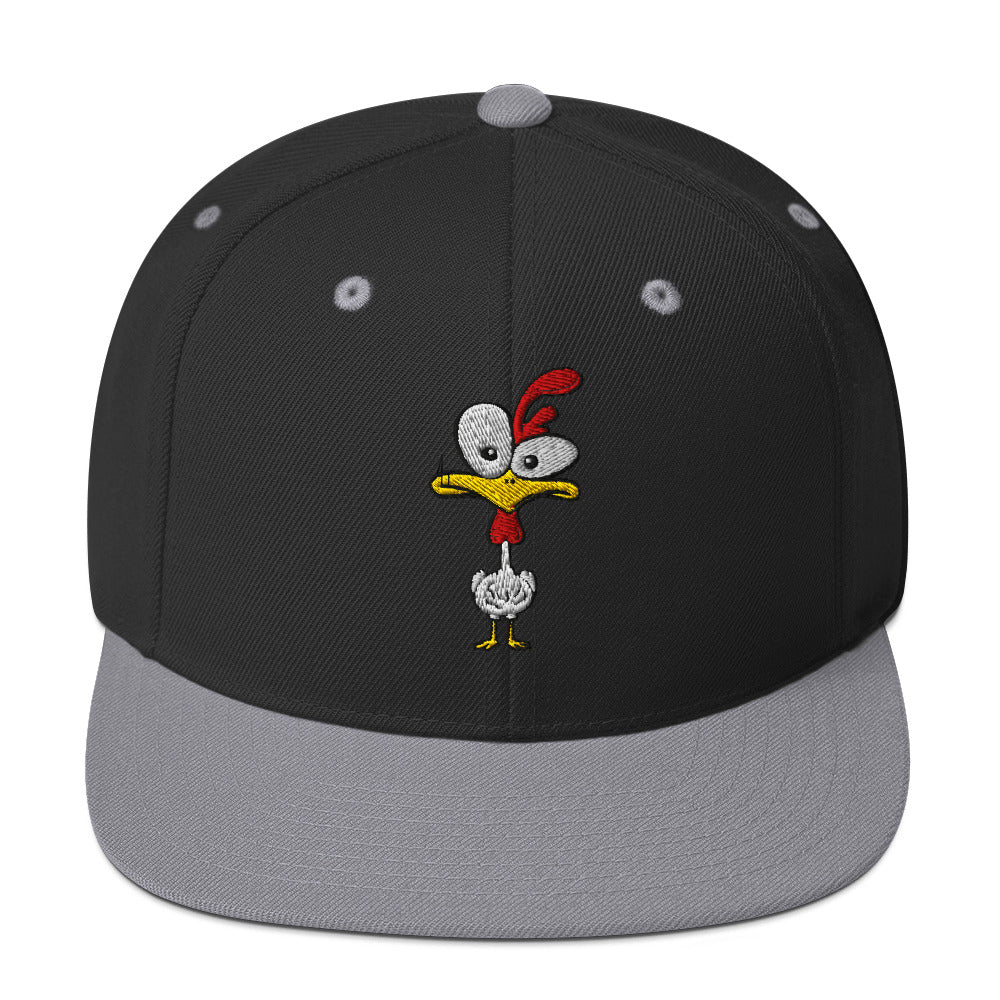 Eine klassische, zweifarbige Snapback-Cap mit flachem Schirm. Auf der Vorderseite ist ein gesticktes Cartoon-Motiv eines Huhns zu sehen, das einen hellen Kopf, große Augen, einen farbigen Kamm und einen Schnabel sowie eine kleine stilisierte Geste am Hals hat. Der obere Teil der Kappe ist dunkel, während der Schirm und der obere Knopf eine leuchtende Kontrastfarbe aufweisen.