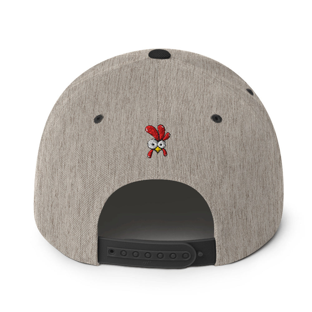 Eine klassische, zweifarbige Snapback-Cap mit flachem Schirm. Auf der Vorderseite ist ein gesticktes Cartoon-Motiv eines Huhns zu sehen, das einen hellen Kopf, große Augen, einen farbigen Kamm und einen Schnabel sowie eine kleine stilisierte Geste am Hals hat. Der obere Teil der Kappe ist dunkel, während der Schirm und der obere Knopf eine leuchtende Kontrastfarbe aufweisen.