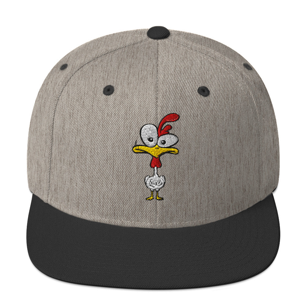 Eine klassische, zweifarbige Snapback-Cap mit flachem Schirm. Auf der Vorderseite ist ein gesticktes Cartoon-Motiv eines Huhns zu sehen, das einen hellen Kopf, große Augen, einen farbigen Kamm und einen Schnabel sowie eine kleine stilisierte Geste am Hals hat. Der obere Teil der Kappe ist dunkel, während der Schirm und der obere Knopf eine leuchtende Kontrastfarbe aufweisen.