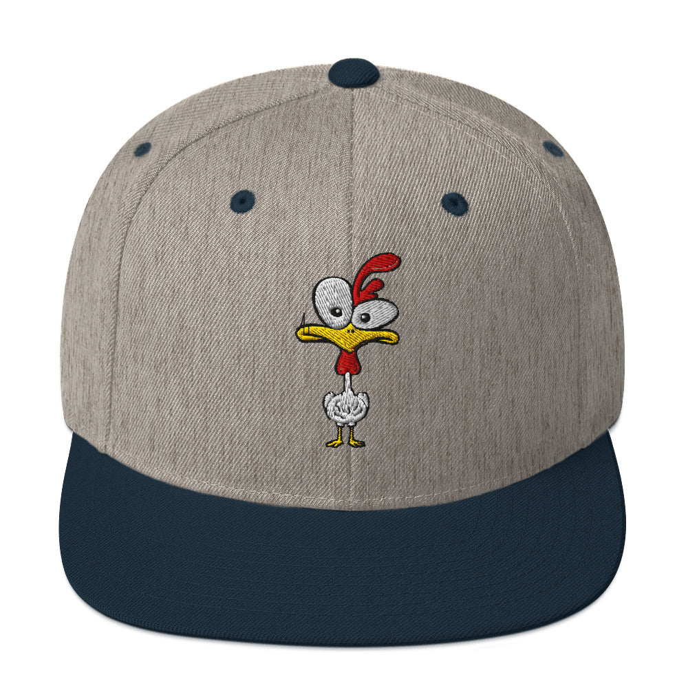 Eine klassische, zweifarbige Snapback-Cap mit flachem Schirm. Auf der Vorderseite ist ein gesticktes Cartoon-Motiv eines Huhns zu sehen, das einen hellen Kopf, große Augen, einen farbigen Kamm und einen Schnabel sowie eine kleine stilisierte Geste am Hals hat. Der obere Teil der Kappe ist dunkel, während der Schirm und der obere Knopf eine leuchtende Kontrastfarbe aufweisen.