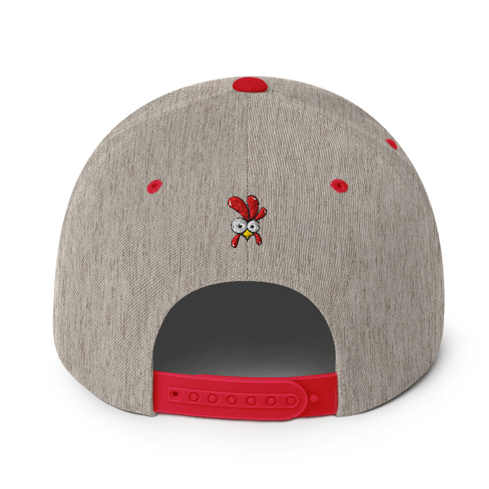 Eine klassische, zweifarbige Snapback-Cap mit flachem Schirm. Auf der Vorderseite ist ein gesticktes Cartoon-Motiv eines Huhns zu sehen, das einen hellen Kopf, große Augen, einen farbigen Kamm und einen Schnabel sowie eine kleine stilisierte Geste am Hals hat. Der obere Teil der Kappe ist dunkel, während der Schirm und der obere Knopf eine leuchtende Kontrastfarbe aufweisen.