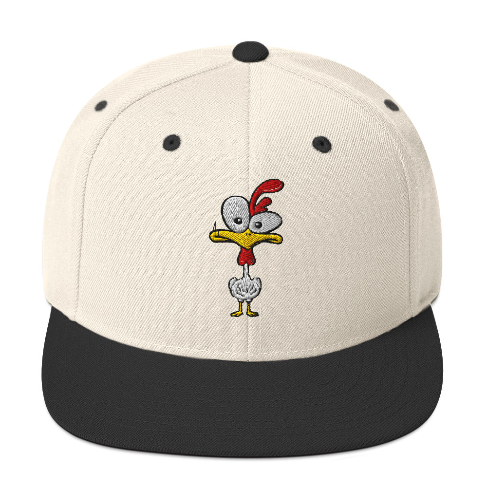Eine klassische, zweifarbige Snapback-Cap mit flachem Schirm. Auf der Vorderseite ist ein gesticktes Cartoon-Motiv eines Huhns zu sehen, das einen hellen Kopf, große Augen, einen farbigen Kamm und einen Schnabel sowie eine kleine stilisierte Geste am Hals hat. Der obere Teil der Kappe ist dunkel, während der Schirm und der obere Knopf eine leuchtende Kontrastfarbe aufweisen.