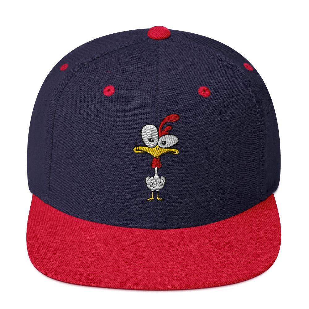 Eine klassische, zweifarbige Snapback-Cap mit flachem Schirm. Auf der Vorderseite ist ein gesticktes Cartoon-Motiv eines Huhns zu sehen, das einen hellen Kopf, große Augen, einen farbigen Kamm und einen Schnabel sowie eine kleine stilisierte Geste am Hals hat. Der obere Teil der Kappe ist dunkel, während der Schirm und der obere Knopf eine leuchtende Kontrastfarbe aufweisen.