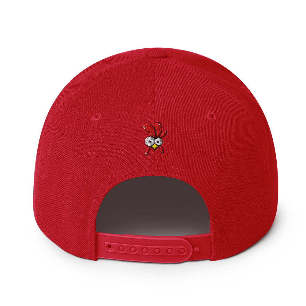 Eine klassische, farbige Snapback-Cap mit flachem Schirm. Auf der Vorderseite ist ein gesticktes Cartoon-Motiv eines Huhns zu sehen, das einen hellen Kopf, große Augen, einen farbigen Kamm und einen Schnabel sowie eine kleine stilisierte Geste am Hals hat. Der obere Teil der Kappe ist dunkel, während der Schirm und der obere Knopf eine leuchtende Kontrastfarbe aufweisen.