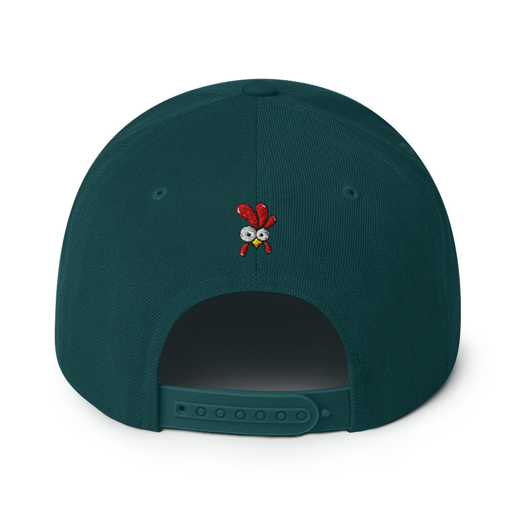 Eine klassische, farbige Snapback-Cap mit flachem Schirm. Auf der Vorderseite ist ein gesticktes Cartoon-Motiv eines Huhns zu sehen, das einen hellen Kopf, große Augen, einen farbigen Kamm und einen Schnabel sowie eine kleine stilisierte Geste am Hals hat. Der obere Teil der Kappe ist dunkel, während der Schirm und der obere Knopf eine leuchtende Kontrastfarbe aufweisen.