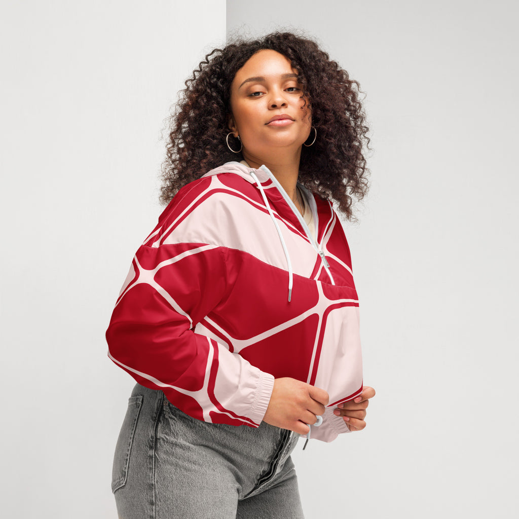 Ein Damen Cropped Windbreaker in Rot und hellem Rosé mit einem abstrakten geometrischen Muster aus miteinander verbundenen, abgerundeten Rechtecken und Linien. Die Jacke hat eine Kapuze, einen halben Reißverschluss, weiße Kordeln und einen verstellbaren Saum. Mockup woman seitliche Ansicht rechts. By Just a Girl.