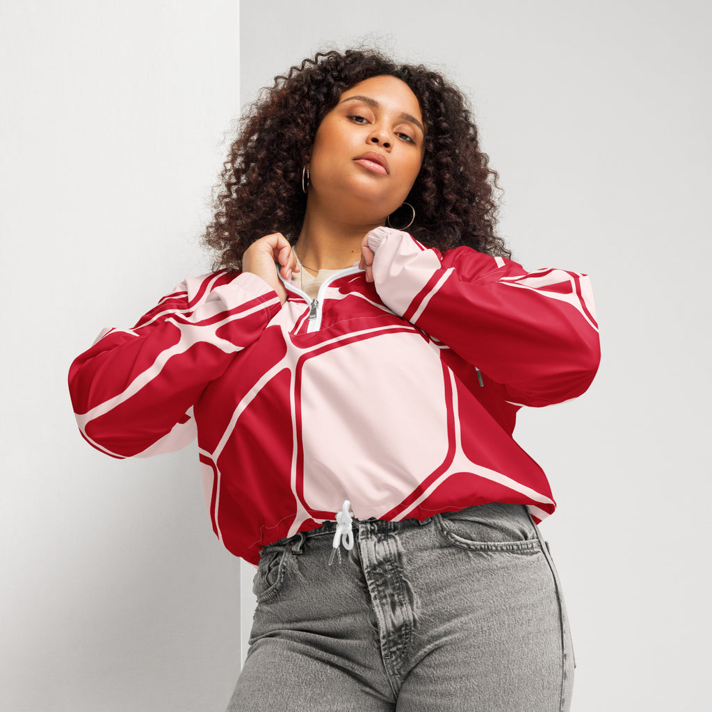 Ein Damen Cropped Windbreaker in Rot und hellem Rosé mit einem abstrakten geometrischen Muster aus miteinander verbundenen, abgerundeten Rechtecken und Linien. Die Jacke hat eine Kapuze, einen halben Reißverschluss, weiße Kordeln und einen verstellbaren Saum. Mockup woman vorder Ansicht. By Just a Girl.