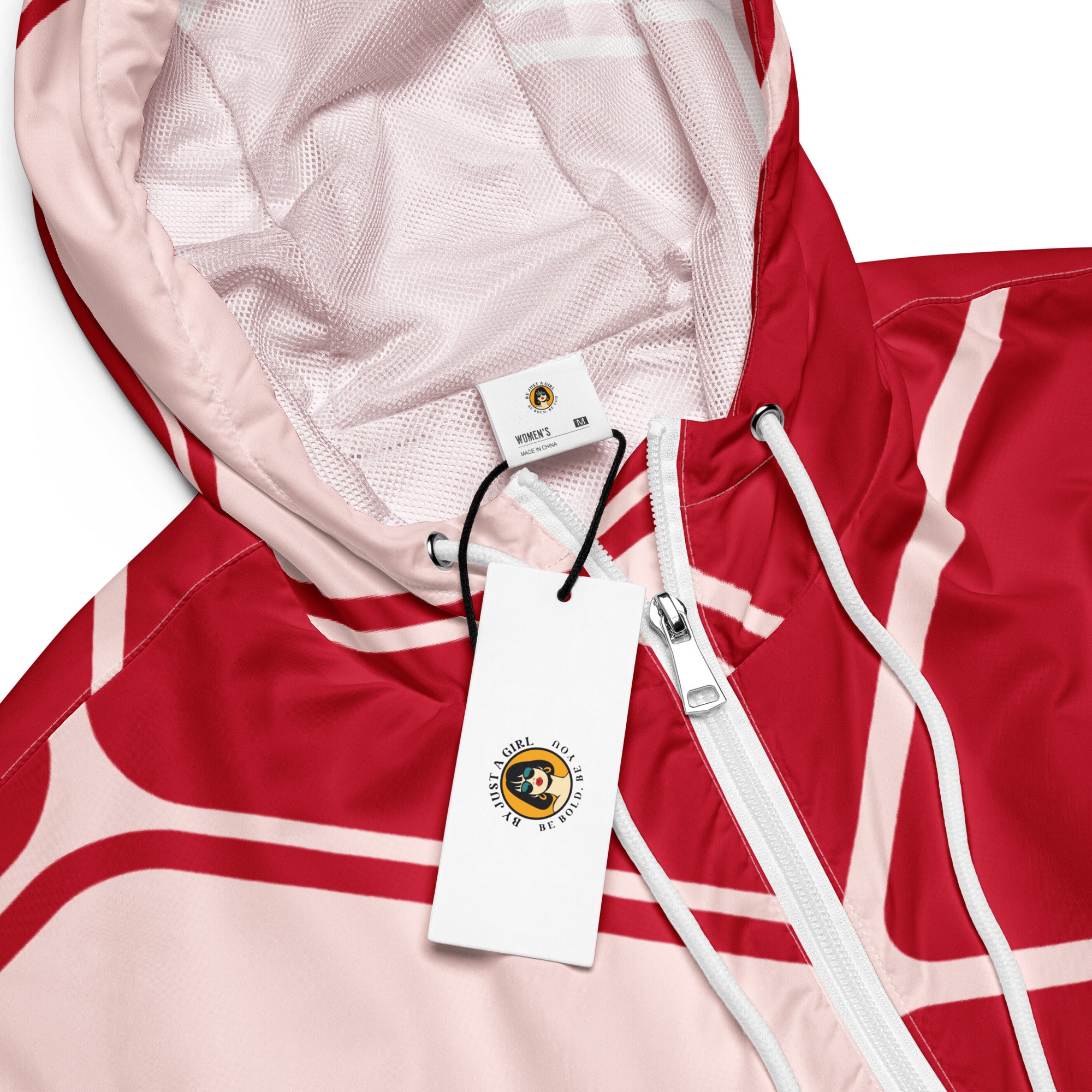Ein Damen Cropped Windbreaker in Rot und hellem Rosé mit einem abstrakten geometrischen Muster aus miteinander verbundenen, abgerundeten Rechtecken und Linien. Die Jacke hat eine Kapuze, einen halben Reißverschluss, weiße Kordeln und einen verstellbaren Saum.  Mockup Kapuzenansicht mit Logo. By Just a Girl.