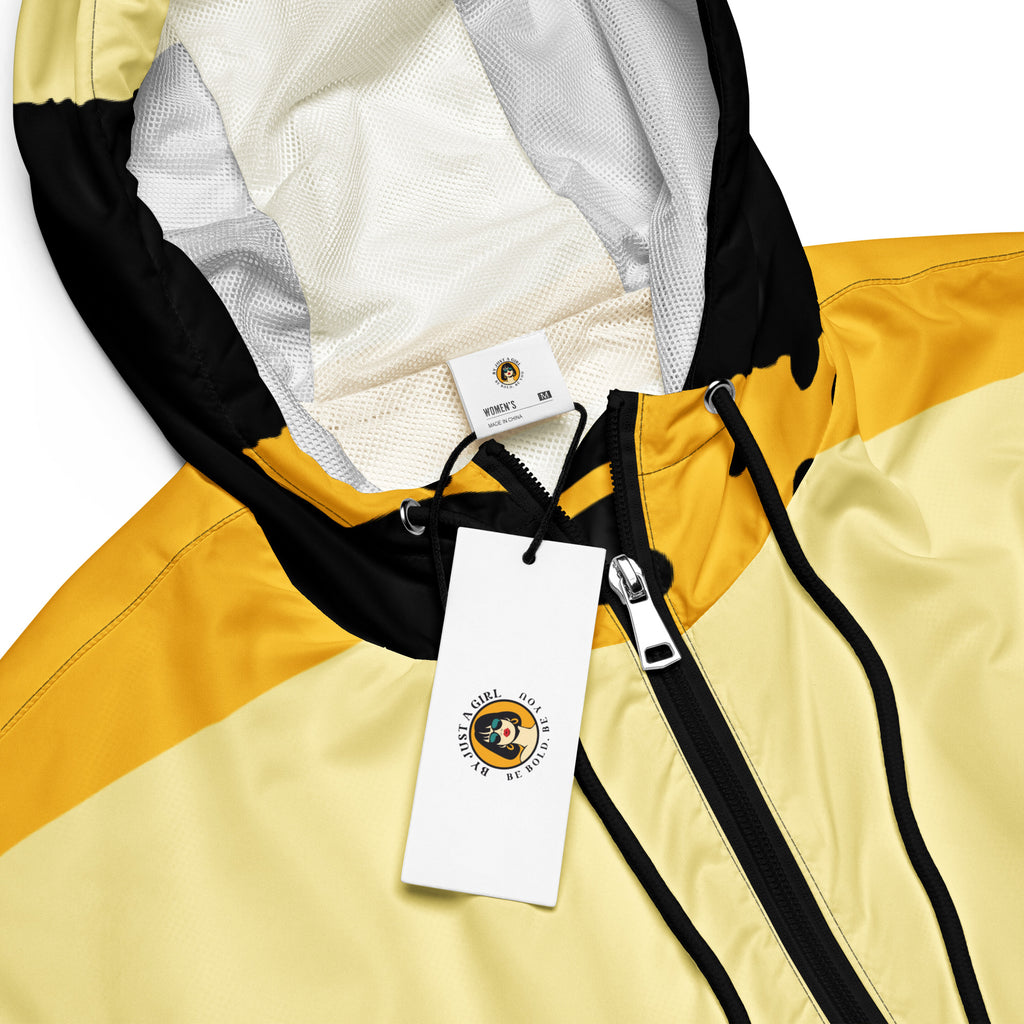 Ein Damen Cropped Windbreaker in Gelb, Schwarz und einem pastell gelb, mit einem auffälligen schwarzen Punktemuster auf der unteren gelben Hälfte. Die Jacke hat eine Kapuze, einen halben Reißverschluss, schwarze Kordeln und einen verstellbaren Saum. By Just a Girl.