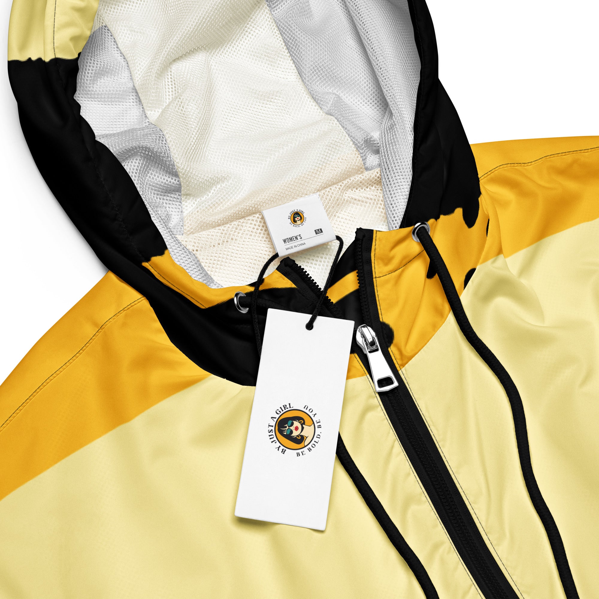 Ein Damen Cropped Windbreaker in Gelb, Schwarz und einem pastell gelb, mit einem auffälligen schwarzen Punktemuster auf der unteren gelben Hälfte. Die Jacke hat eine Kapuze, einen halben Reißverschluss, schwarze Kordeln und einen verstellbaren Saum. By Just a Girl.