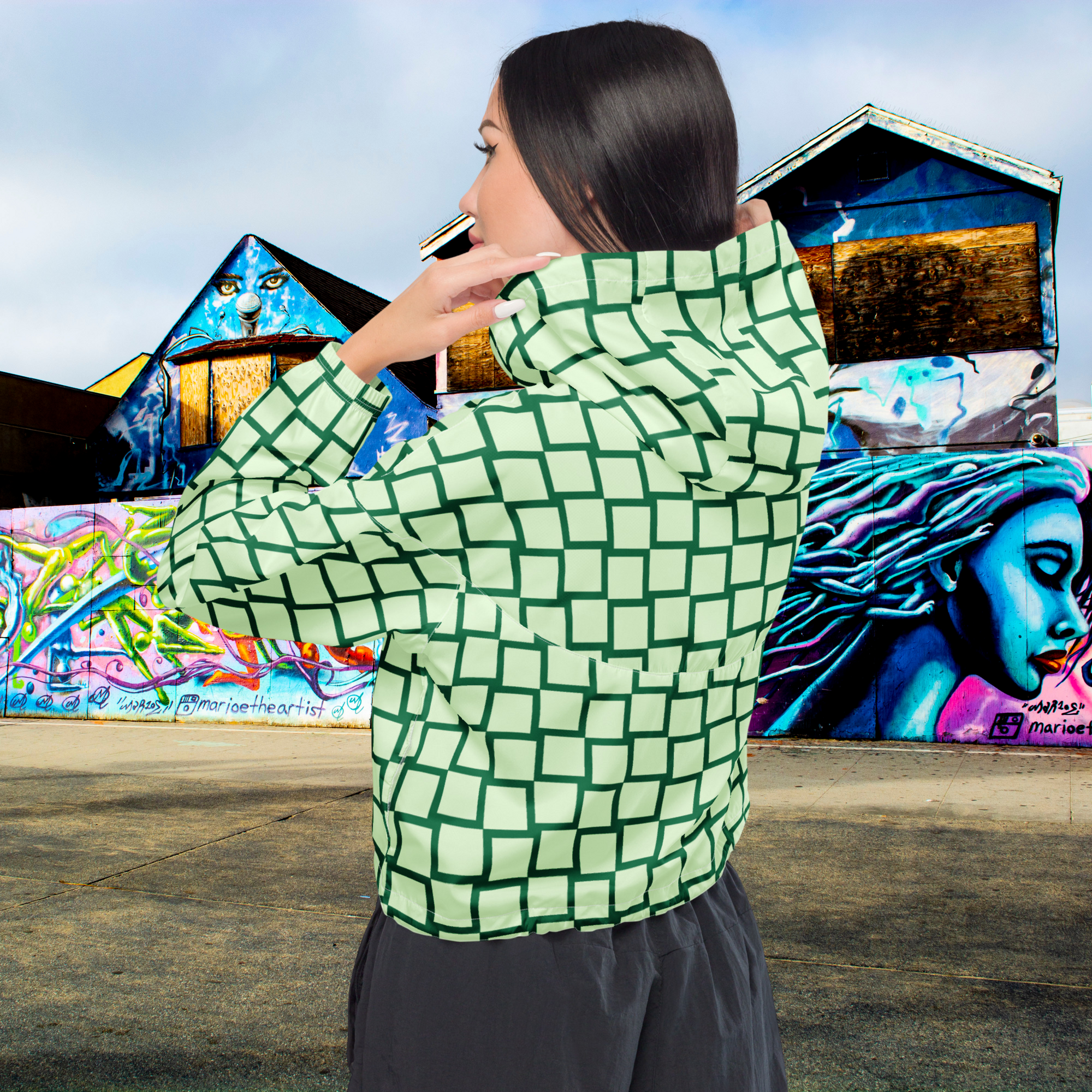 Ein Damen Cropped Windbreaker mit einem Schachbrettmuster in hellem Mintgrün und dunklem Grün. Die Jacke hat eine Kapuze, einen halben Reißverschluss mit weißen Kordeln und einen verstellbaren Saum. Mockup Girl Rückenansicht. By Just a Girl.
