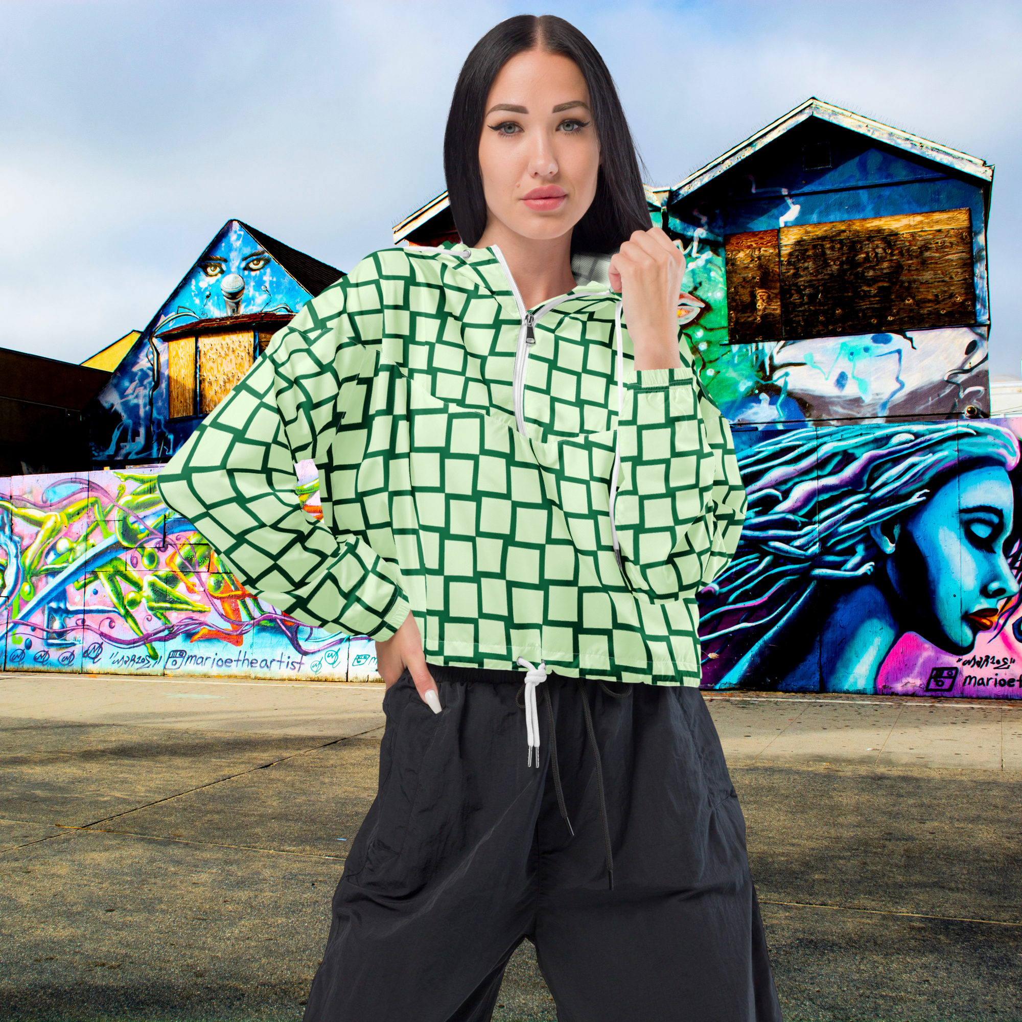 Ein Damen Cropped Windbreaker mit einem Schachbrettmuster in hellem Mintgrün und dunklem Grün. Die Jacke hat eine Kapuze, einen halben Reißverschluss mit weißen Kordeln und einen verstellbaren Saum. Mockup Girl Vorderansicht. By Just a Girl.