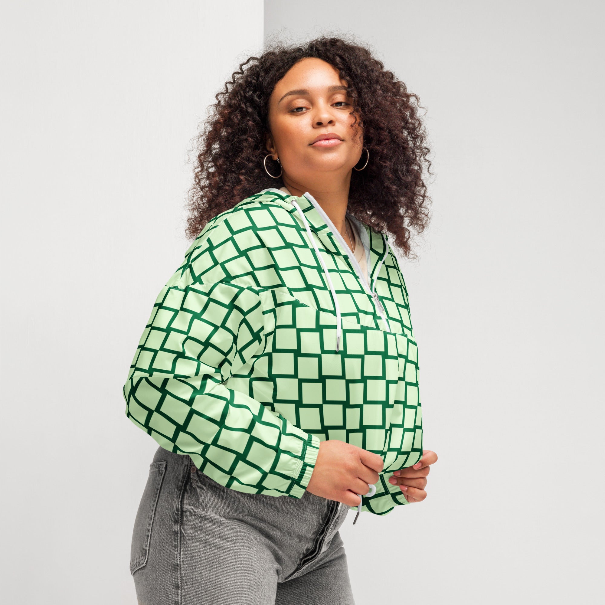 Ein Damen Cropped Windbreaker mit einem Schachbrettmuster in hellem Mintgrün und dunklem Grün. Die Jacke hat eine Kapuze, einen halben Reißverschluss mit weißen Kordeln und einen verstellbaren Saum. Mockup woman seitliche Ansicht rechts.  By Just a Girl.