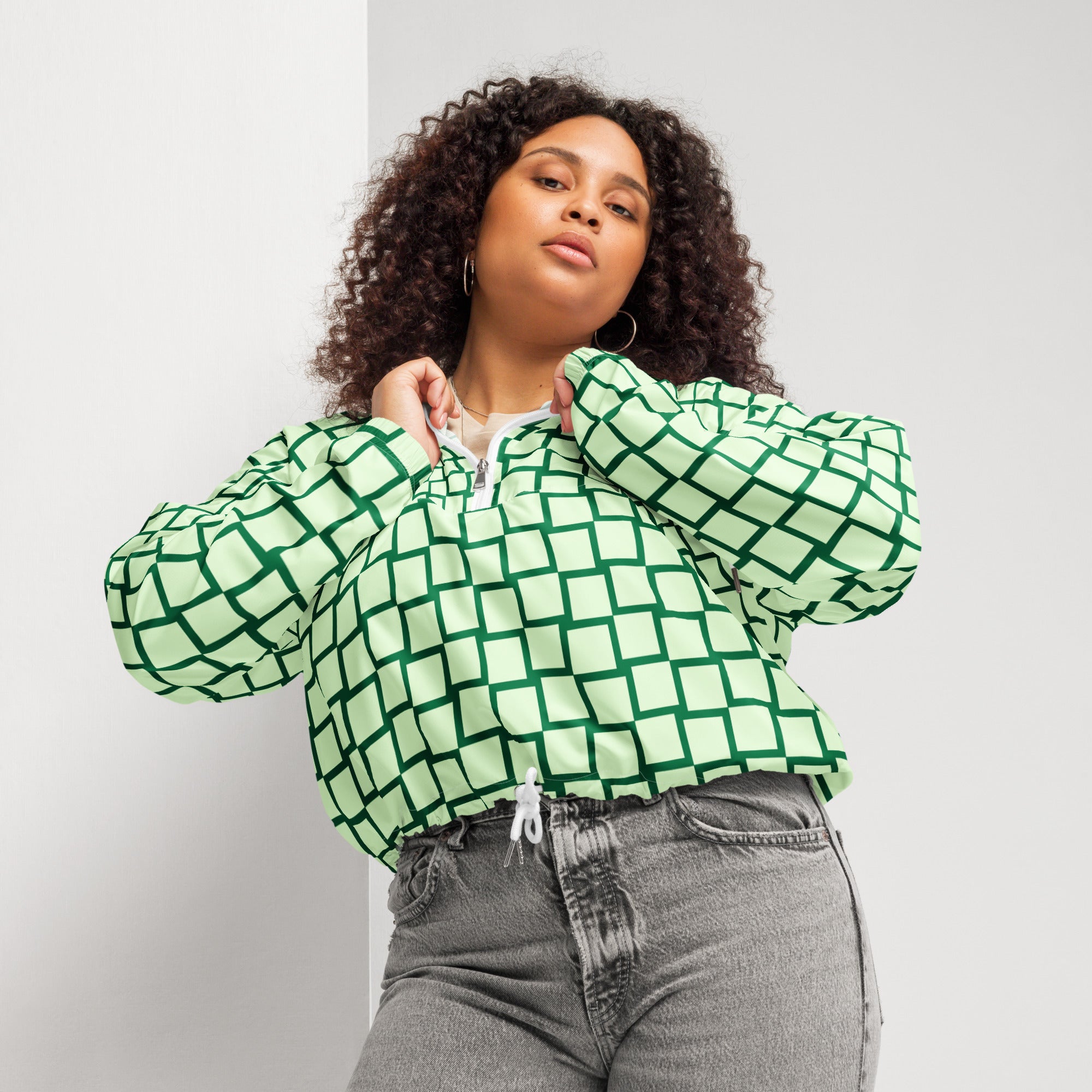 Ein Damen Cropped Windbreaker mit einem Schachbrettmuster in hellem Mintgrün und dunklem Grün. Die Jacke hat eine Kapuze, einen halben Reißverschluss mit weißen Kordeln und einen verstellbaren Saum. Mockup woman Vorderansicht. By Just a Girl.