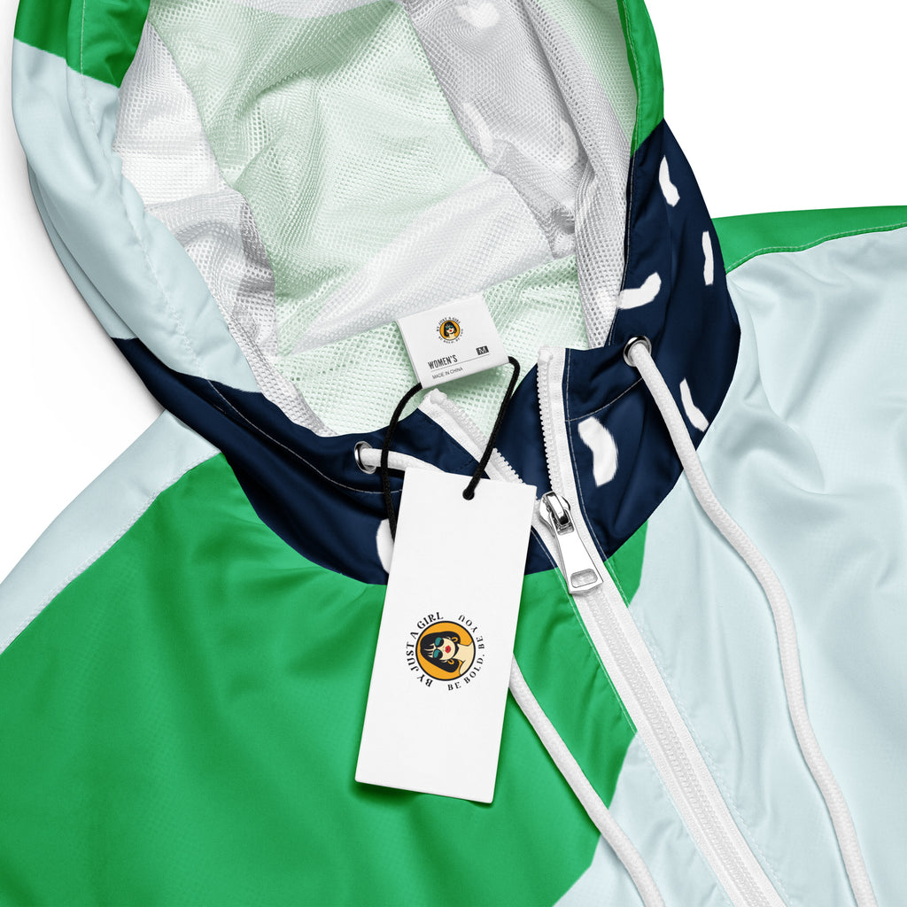 Ein Damen Cropped Windbreaker mit einem modernen, geometrischen Blockmuster in Dunkelblau, hellem Mintgrün und strahlendem Grün. Der dunkelblaue Bereich ist zusätzlich mit kleinen weißen, unregelmäßigen Strichformen versehen. Die Jacke hat eine Kapuze, einen halben Reißverschluss mit weißen Kordeln und einen verstellbaren Saum. Mockup Kapuzen Ansicht mit logo. By Just a Girl.