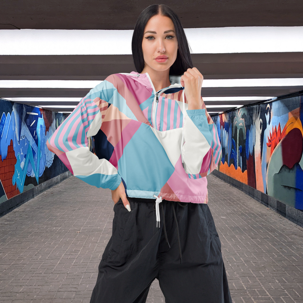 Ein Damen Cropped Windbreaker mit einem lebhaften, geometrischen Muster aus verschiedenen Dreiecken und Rechtecken in Pastellfarben wie Hellblau, Rosa, Beige, Dunkelblau und Weiß. Die Jacke hat eine Kapuze, einen halben Reißverschluss, weiße Kordeln und einen verstellbaren Saum. Mockup Girl Vorderseite.  By Just a Girl.