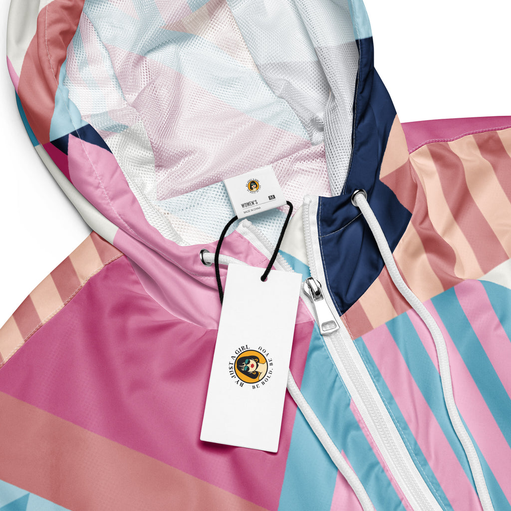 Ein Damen Cropped Windbreaker mit einem lebhaften, geometrischen Muster aus verschiedenen Dreiecken und Rechtecken in Pastellfarben wie Hellblau, Rosa, Beige, Dunkelblau und Weiß. Die Jacke hat eine Kapuze, einen halben Reißverschluss, weiße Kordeln und einen verstellbaren Saum. Kopf ansicht mit Logo. By Just a Girl.