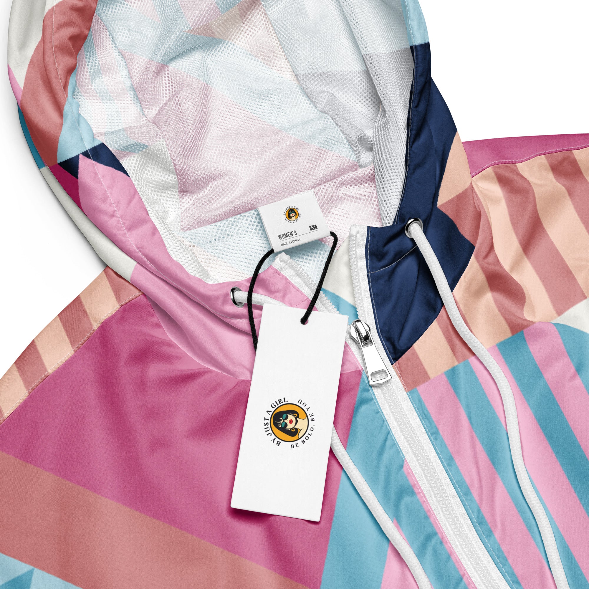 Ein Damen Cropped Windbreaker mit einem lebhaften, geometrischen Muster aus verschiedenen Dreiecken und Rechtecken in Pastellfarben wie Hellblau, Rosa, Beige, Dunkelblau und Weiß. Die Jacke hat eine Kapuze, einen halben Reißverschluss, weiße Kordeln und einen verstellbaren Saum. Kopf ansicht mit Logo. By Just a Girl.