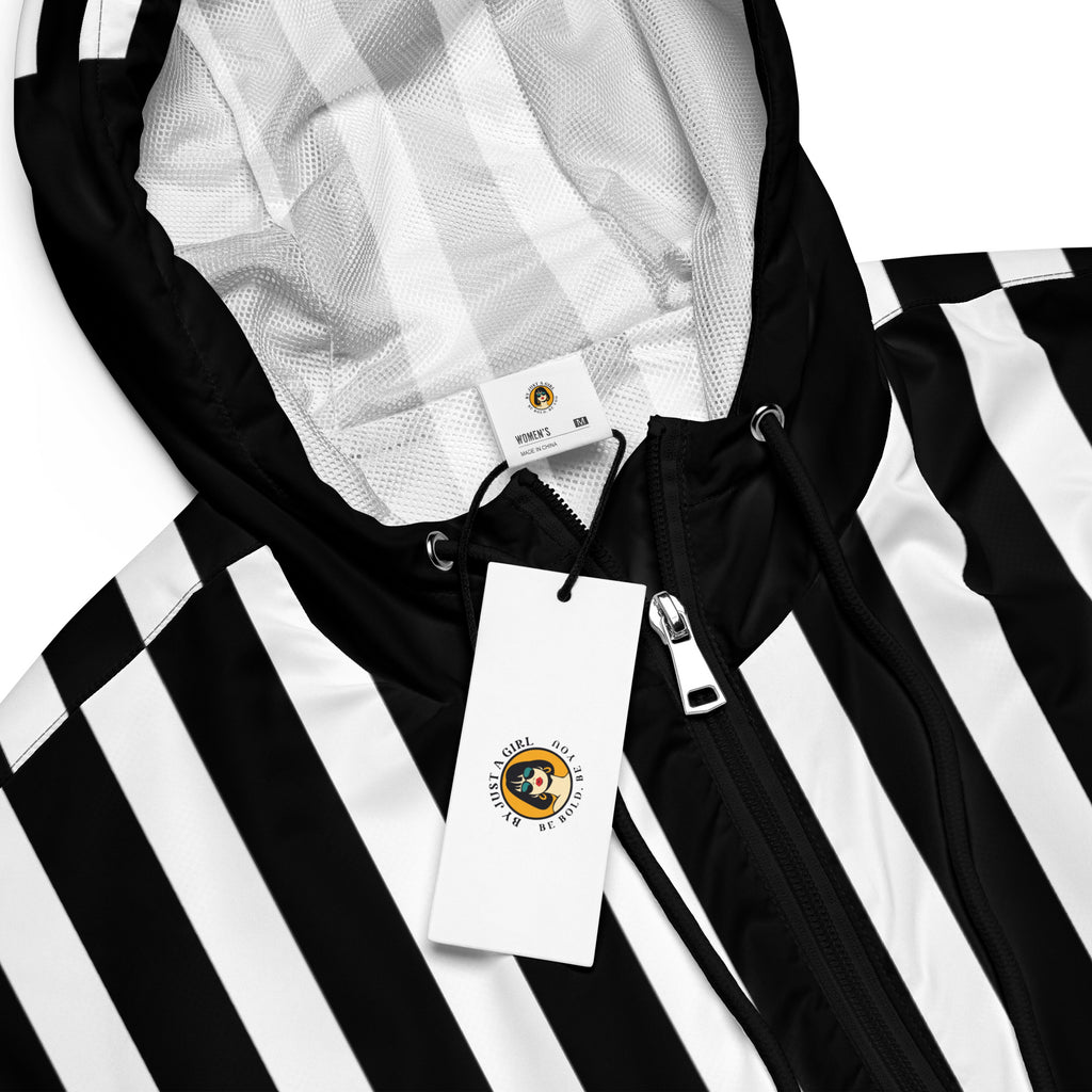 Ein Damen Cropped Windbreaker in Schwarz und Weiß mit einem markanten vertikalen und horizontalen Streifenmuster. Der obere Bereich und die Kapuze zeigen vertikale Streifen, während die Mitte schwarz ist und die untere Hälfte breite horizontale Streifen aufweist. Die Jacke hat einen halben Reißverschluss, schwarze Kordeln und einen verstellbaren Saum.  By Just a Girl.