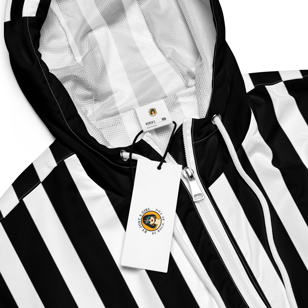 Ein Damen Cropped Windbreaker in Schwarz und Weiß mit einem markanten vertikalen und horizontalen Streifenmuster. Der obere Bereich und die Kapuze zeigen vertikale Streifen, während die Mitte schwarz ist und die untere Hälfte breite horizontale Streifen aufweist. Die Jacke hat einen halben Reißverschluss, schwarze Kordeln und einen verstellbaren Saum. Mockup Girl vordere ansicht By Just a Girl.