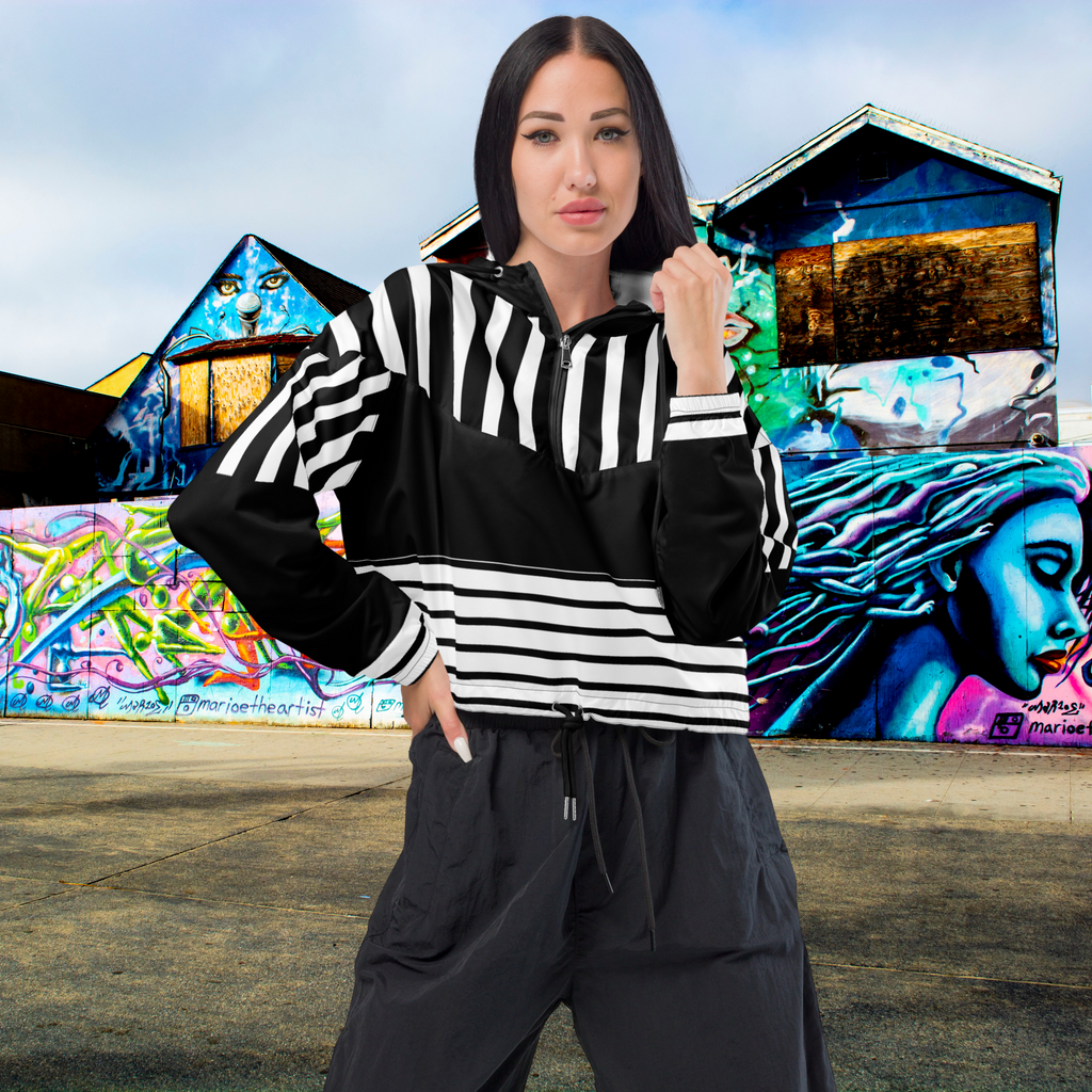 Ein Damen Cropped Windbreaker in Schwarz und Weiß mit einem markanten vertikalen und horizontalen Streifenmuster. Der obere Bereich und die Kapuze zeigen vertikale Streifen, während die Mitte schwarz ist und die untere Hälfte breite horizontale Streifen aufweist. Die Jacke hat einen halben Reißverschluss, schwarze Kordeln und einen verstellbaren Saum. Mockup Girl vordere ansicht By Just a Girl.