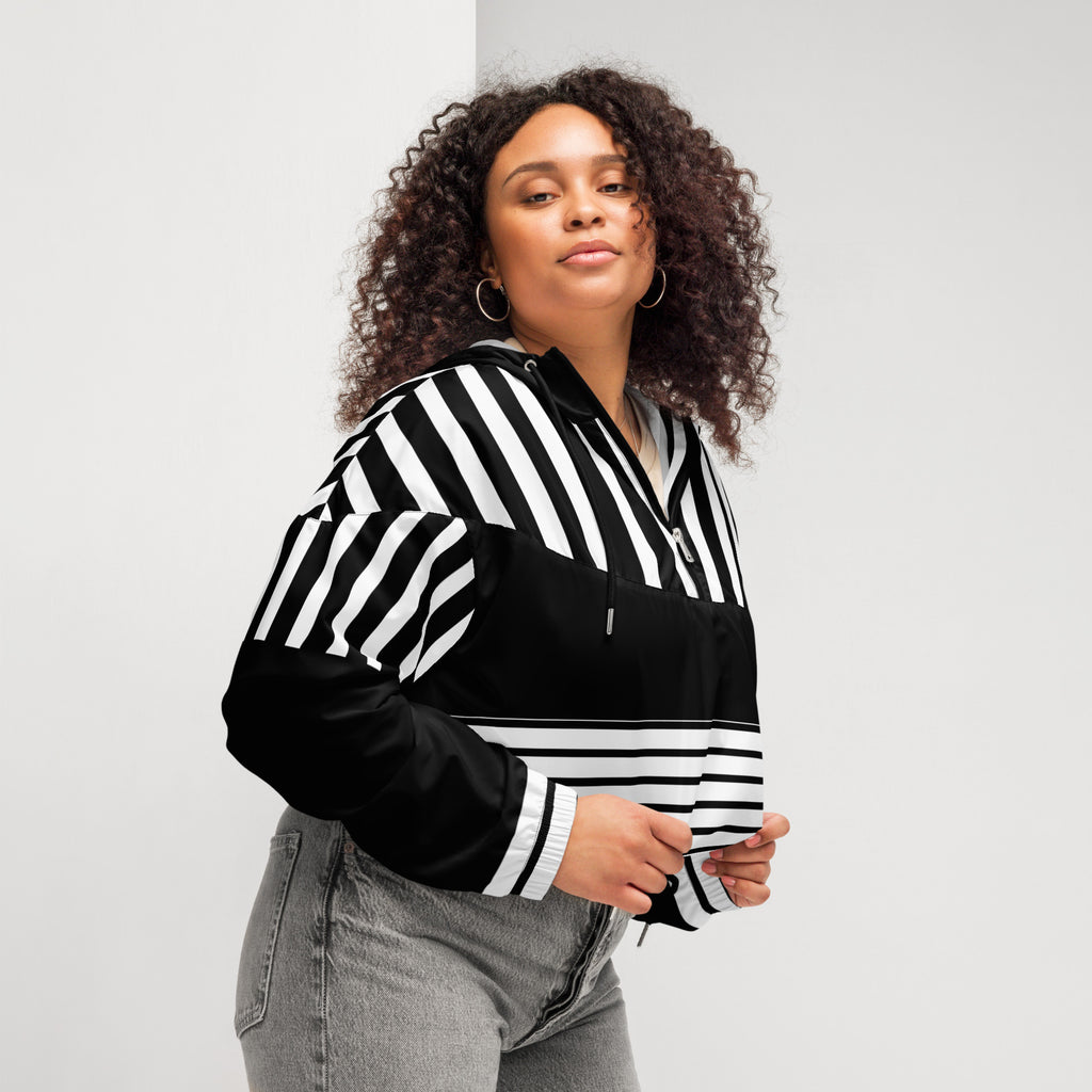 Ein Damen Cropped Windbreaker in Schwarz und Weiß mit einem markanten vertikalen und horizontalen Streifenmuster. Der obere Bereich und die Kapuze zeigen vertikale Streifen, während die Mitte schwarz ist und die untere Hälfte breite horizontale Streifen aufweist. Die Jacke hat einen halben Reißverschluss, schwarze Kordeln und einen verstellbaren Saum. Mockup woman rechte seiten ansicht By Just a Girl.