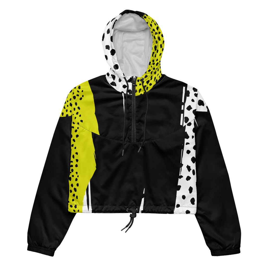 Ein Damen Cropped Windbreaker in Schwarz, Gelb und Weiß mit einem auffälligen, asymmetrischen Muster aus großen gelben Formen mit schwarzen Punkten, schwarzen Segmenten und weißen Bereichen mit schwarzen Punkten. Die Jacke hat eine Kapuze mit gelb-weißem Muster, einen halben Reißverschluss, schwarze Kordeln und einen verstellbaren Saum. By Just a Girl