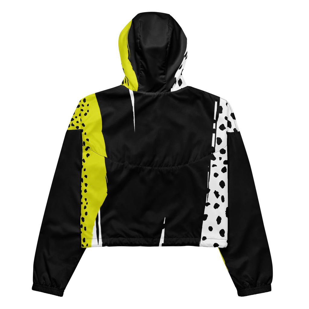 Ein Damen Cropped Windbreaker in Schwarz, Gelb und Weiß mit einem auffälligen, asymmetrischen Muster aus großen gelben Formen mit schwarzen Punkten, schwarzen Segmenten und weißen Bereichen mit schwarzen Punkten. Die Jacke hat eine Kapuze mit gelb-weißem Muster, einen halben Reißverschluss, schwarze Kordeln und einen verstellbaren Saum. By Just a Girl