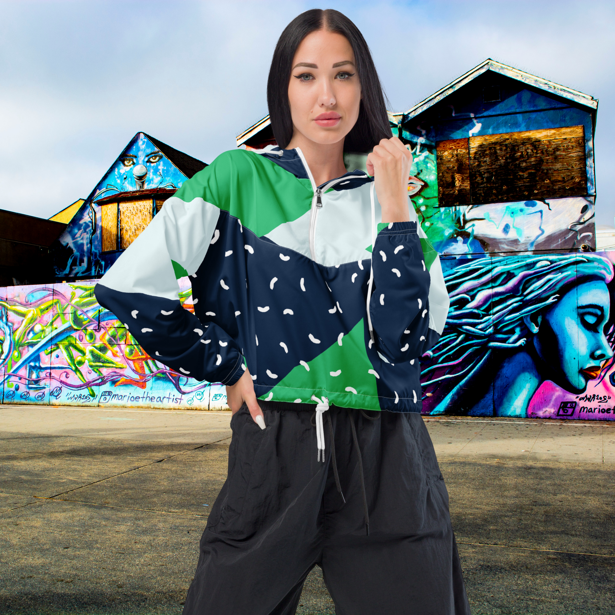 Ein Damen Cropped Windbreaker mit einem modernen, geometrischen Blockmuster in Dunkelblau, hellem Mintgrün und strahlendem Grün. Der dunkelblaue Bereich ist zusätzlich mit kleinen weißen, unregelmäßigen Strichformen versehen. Die Jacke hat eine Kapuze, einen halben Reißverschluss mit weißen Kordeln und einen verstellbaren Saum. Mockup Girl Vorderansicht. By Just a Girl.