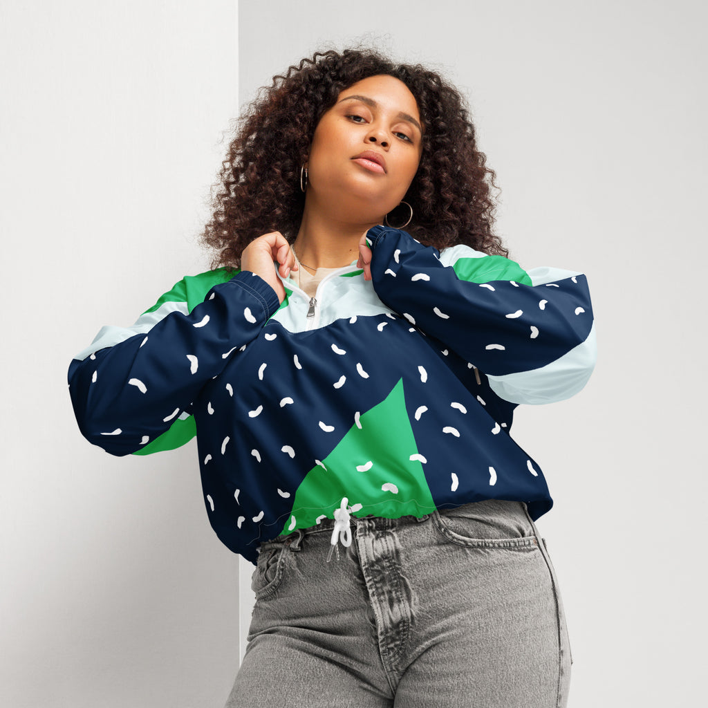 Ein Damen Cropped Windbreaker mit einem modernen, geometrischen Blockmuster in Dunkelblau, hellem Mintgrün und strahlendem Grün. Der dunkelblaue Bereich ist zusätzlich mit kleinen weißen, unregelmäßigen Strichformen versehen. Die Jacke hat eine Kapuze, einen halben Reißverschluss mit weißen Kordeln und einen verstellbaren Saum. Mockup woman Vorderansicht. By Just a Girl.