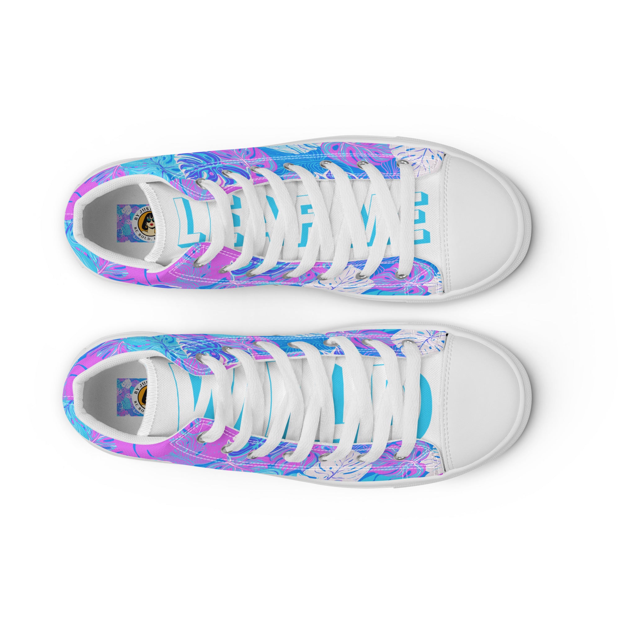 Ansicht von oben der  High-Top-Canvas-Sneaker mit einem Muster aus tropischen Blättern in Blau, Lila und Pink. Die Sohlen, Zehenkappen und Schnürsenkel sind weiß. Die weißen Schuhzungen sind mit blauem Text "Leaf me" auf dem einen Schuh und "Wild" auf dem anderen beschriftet. Designed, by Just a Girl.