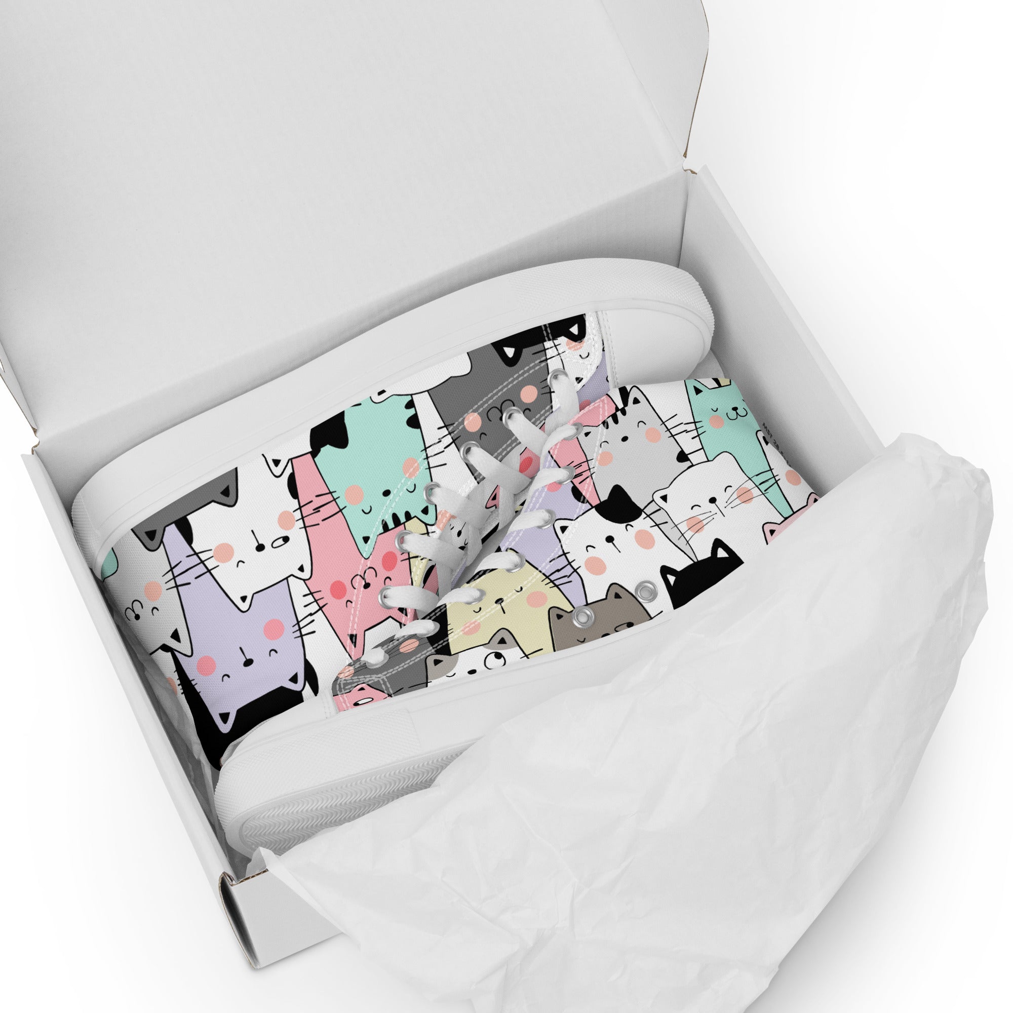 Ansicht liegend im Schuhkarton der weißen High-Top-Sneaker mit einem dichten Muster aus verschiedenfarbigen Cartoon-Katzenköpfen. Die Katzen sind in Pastelltönen wie Rosa, Hellblau, Grau und Violett gehalten. Die Schnürsenkel und Zehenkappen sind weiß. Designed, by Just a Girl.