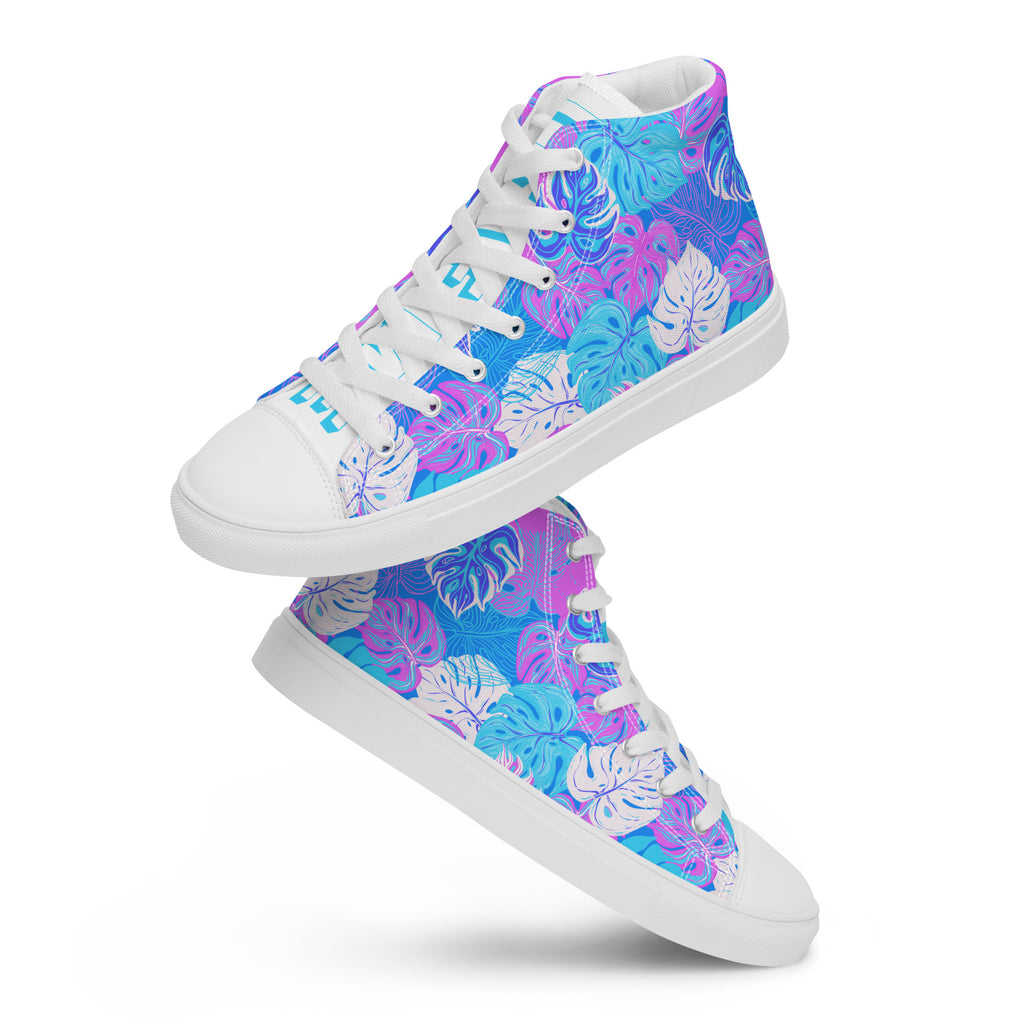 Ein Paar schwebende High-Top-Canvas-Sneaker mit einem Muster aus tropischen Blättern in Blau, Lila und Pink. Die Sohlen, Zehenkappen und Schnürsenkel sind weiß. Die weißen Schuhzungen sind mit blauem Text "Leaf me" auf dem einen Schuh und "Wild" auf dem anderen beschriftet. Designed, by Just a Girl.