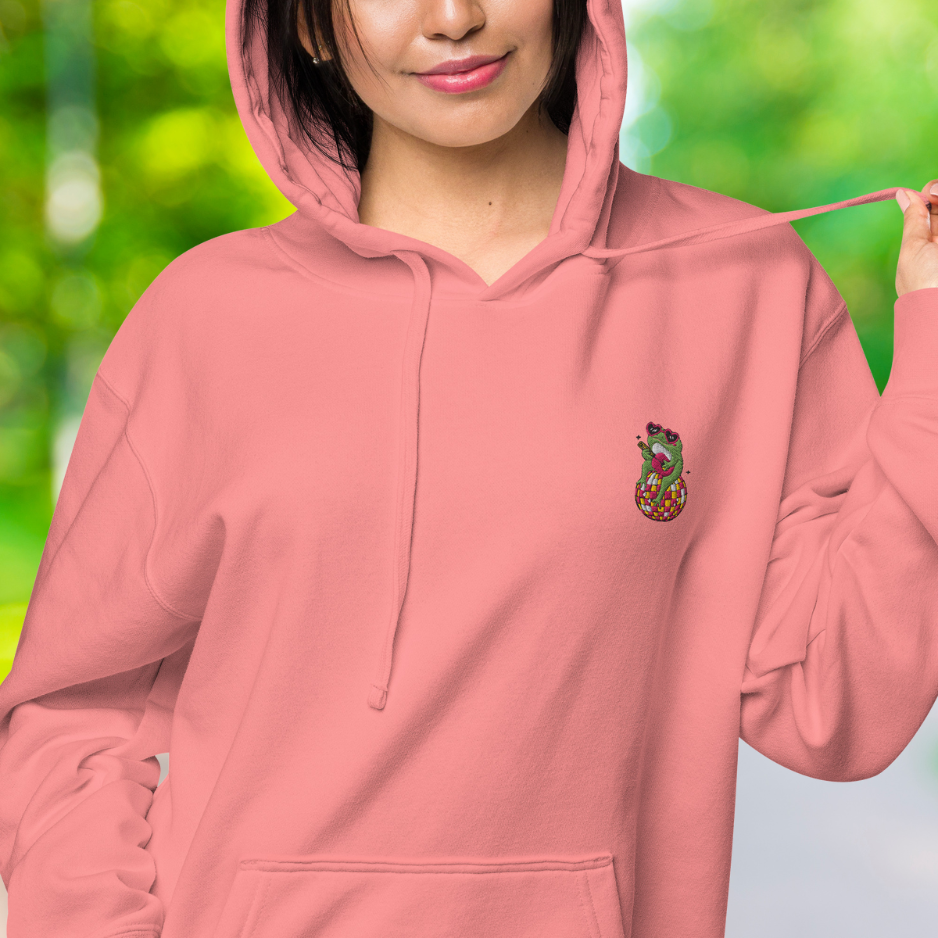 Nahaufnahme des weiblichen Models mit Sicht auf das gestickte Happy Frog Emblem auf der linken Brusthöhe. Designed, by Just a Girl