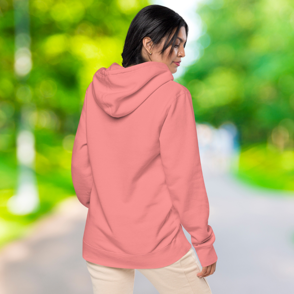 Ein weibliches Model zeigt sich draußen im freien mit den Pigment pinken Kapuzenpullover von der Rückseite.