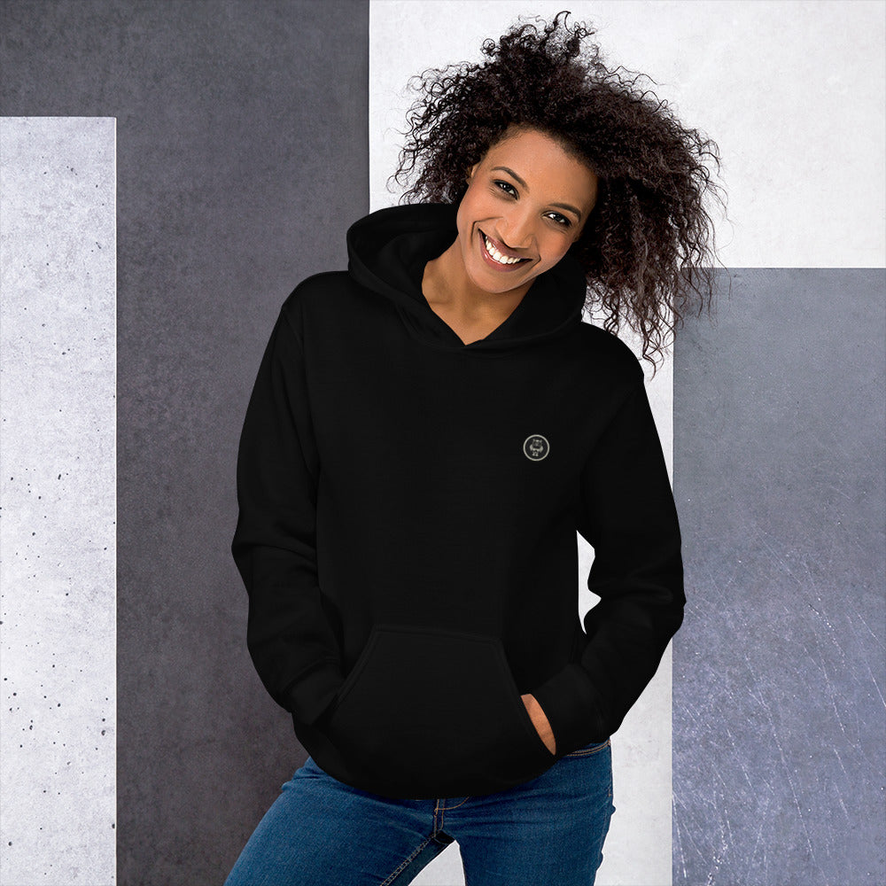 Ein weibliches Model zeigt sich mit dem Kapuzenpullover "The Black One" Beide Hände lässig in der vorderen Beuteltasche.